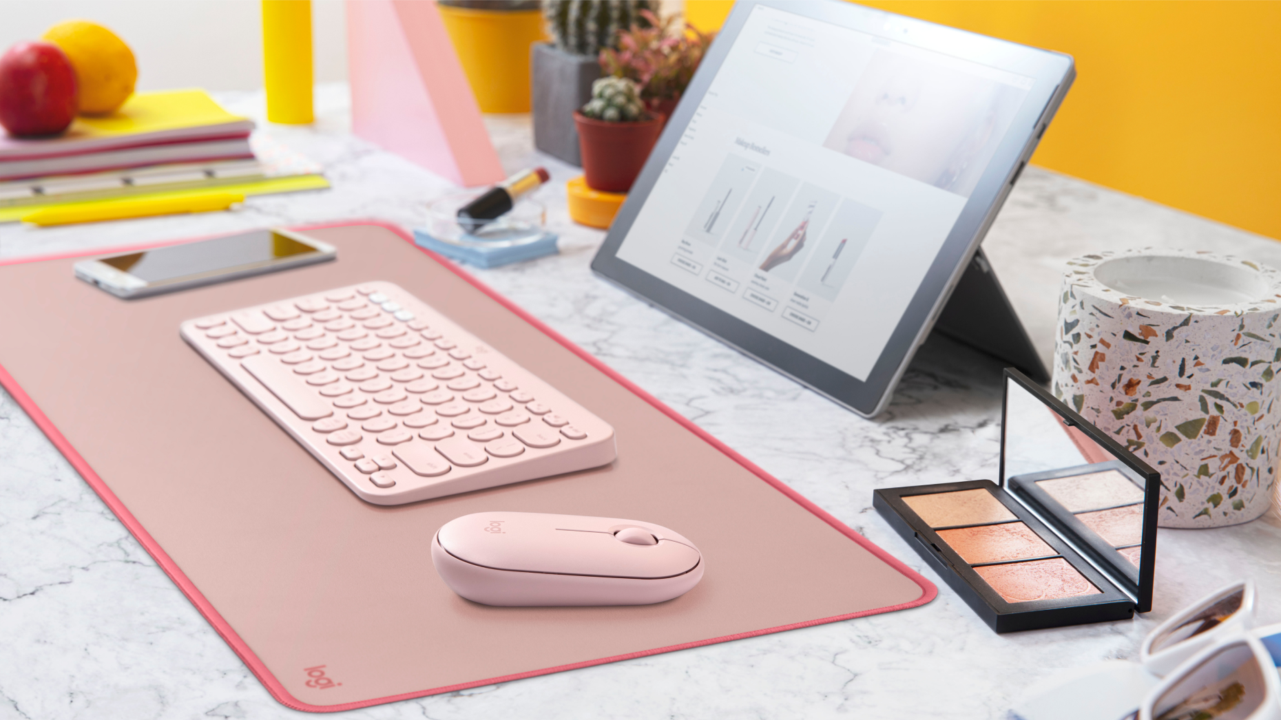 Configuration de bureau rose avec clavier, souris et tablette, avec maquillage.