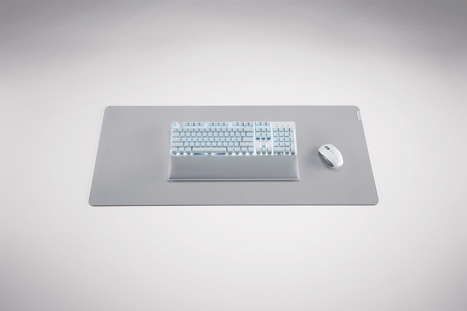 Eine Tastatur, Maus und Handgelenkstütze auf einem großen grauen Mousepad, alles auf weißem Untergrund.