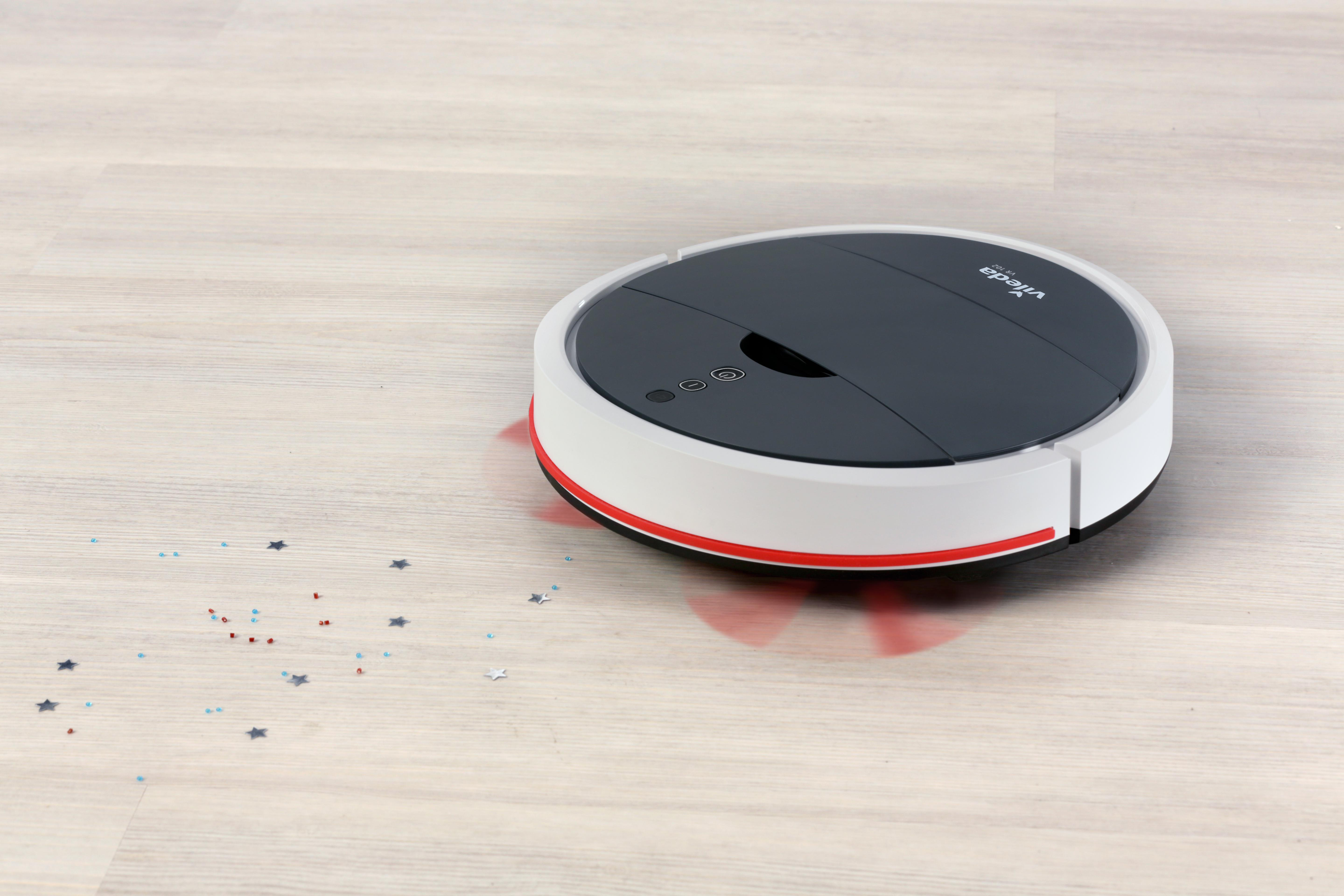 Ein Roboter-Staubsauger auf hellem Holzboden mit verstreutem Konfetti.
