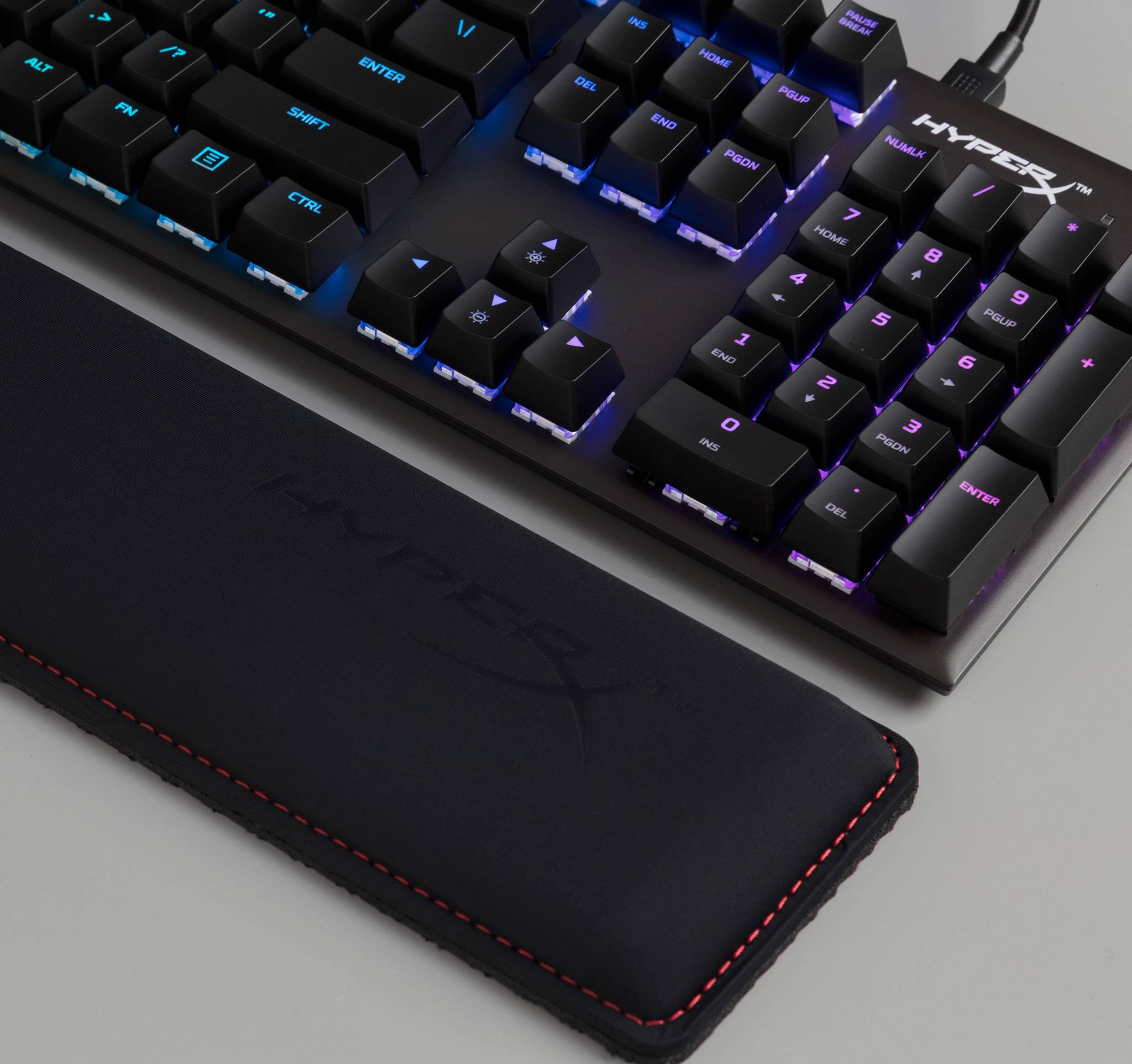 Schwarze HyperX-Tastatur mit beleuchteten Tasten, Handgelenkauflage und roten Nähten.