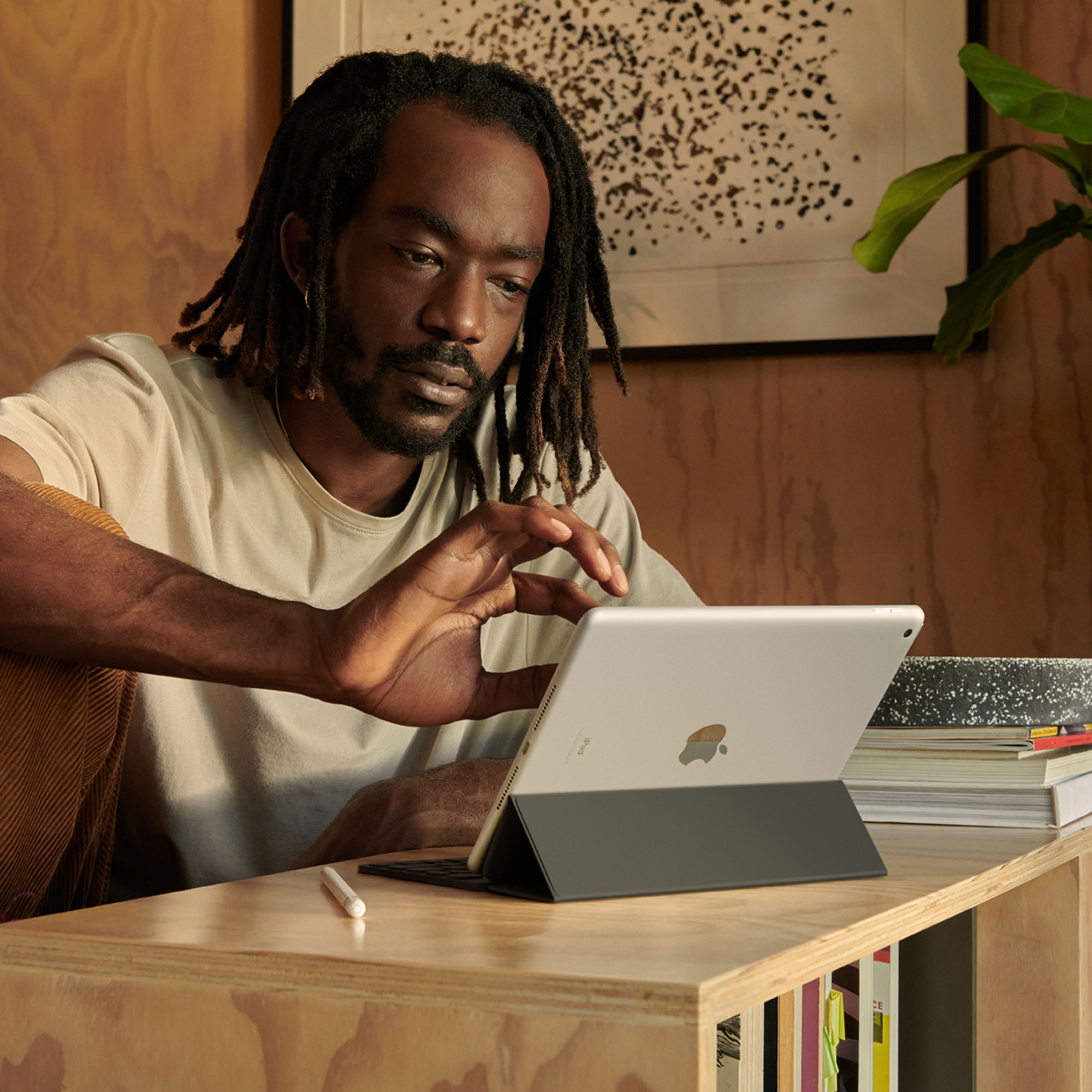 Un hombre con rastas usando una tableta con teclado en un escritorio de madera.