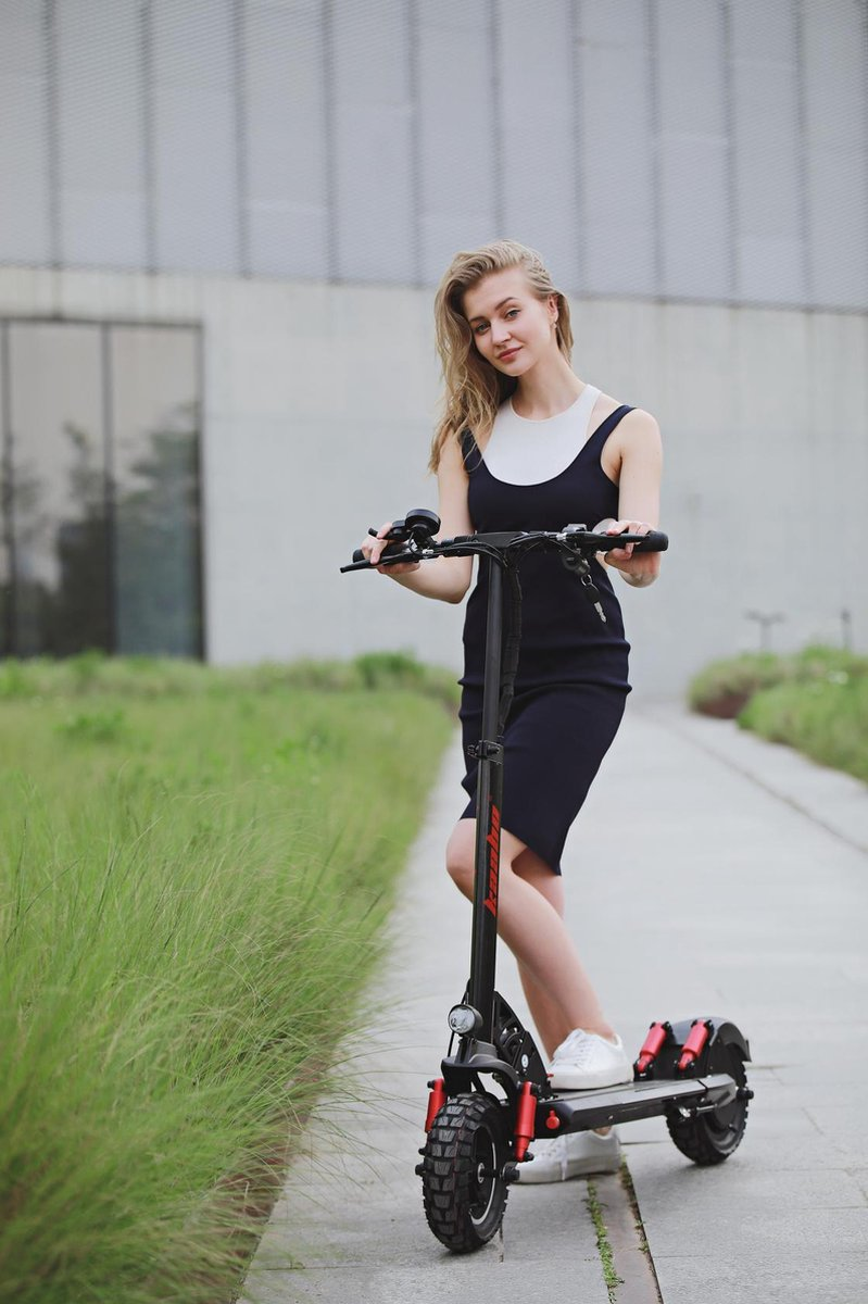 Une femme sur un scooter, portant une robe, posant sur un chemin.