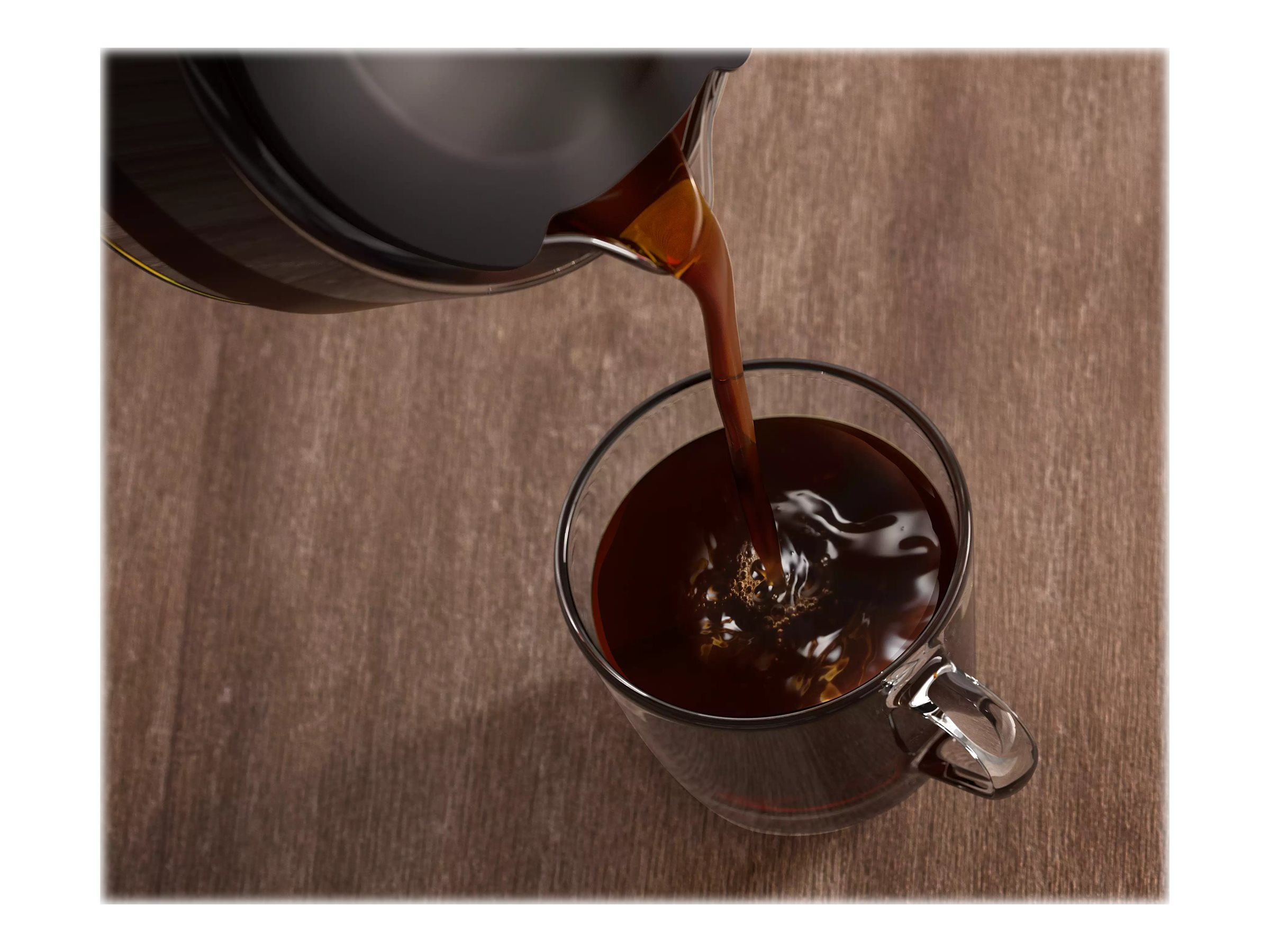 Kaffee wird aus einer schwarzen Karaffe in eine transparente Glastasse auf einer Holzoberfläche gegossen.