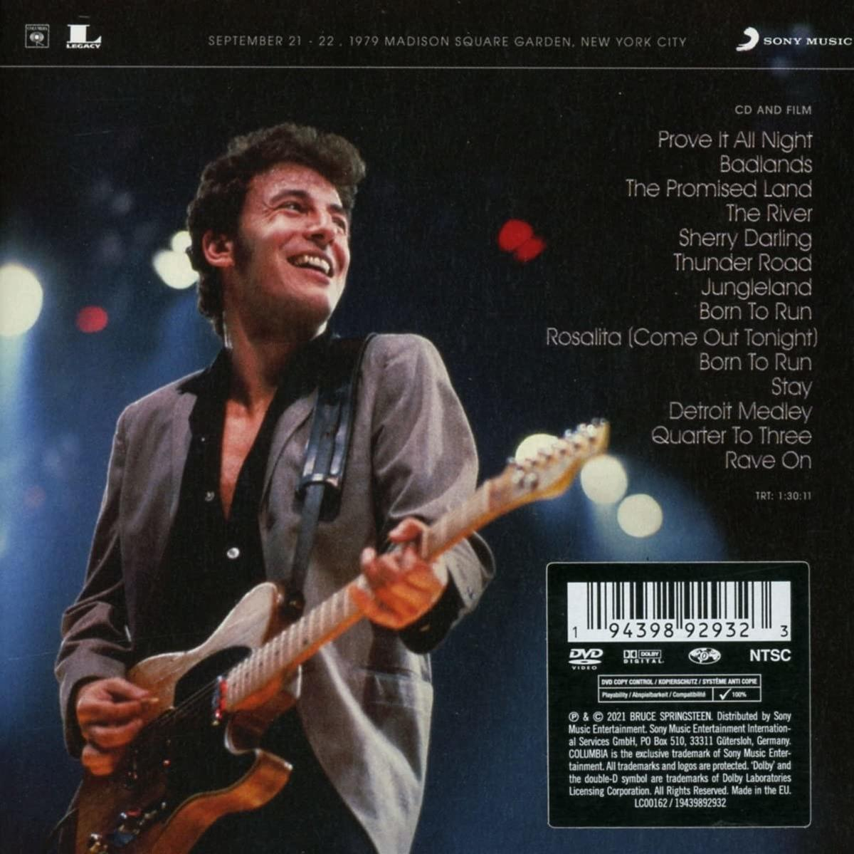 Un homme jouant de la guitare sur scène avec un groupe, avec la couverture du DVD dans le coin.
