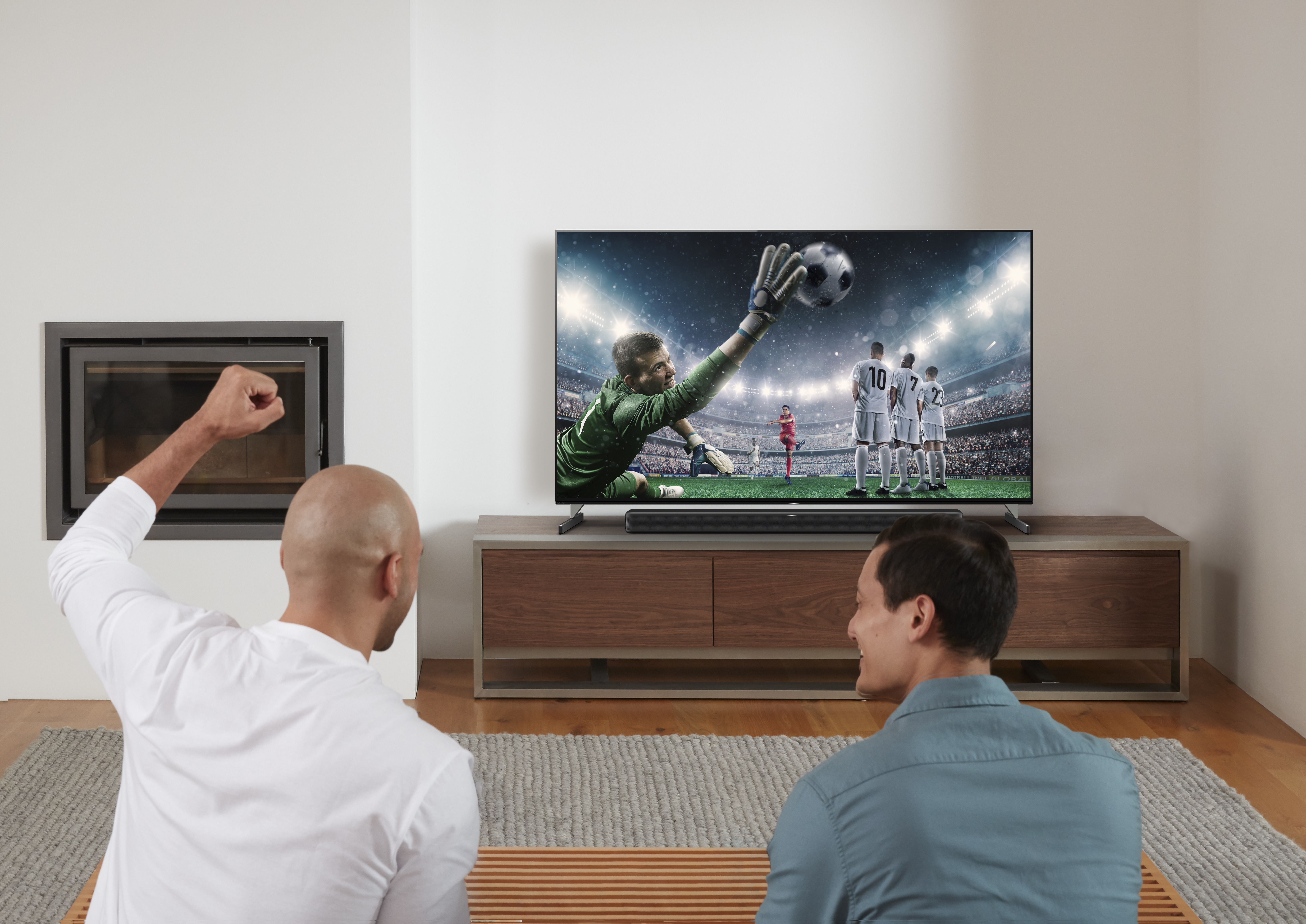 Zwei Männer schauen ein Fußballspiel im Fernsehen, einer jubelt mit erhobenem Arm.