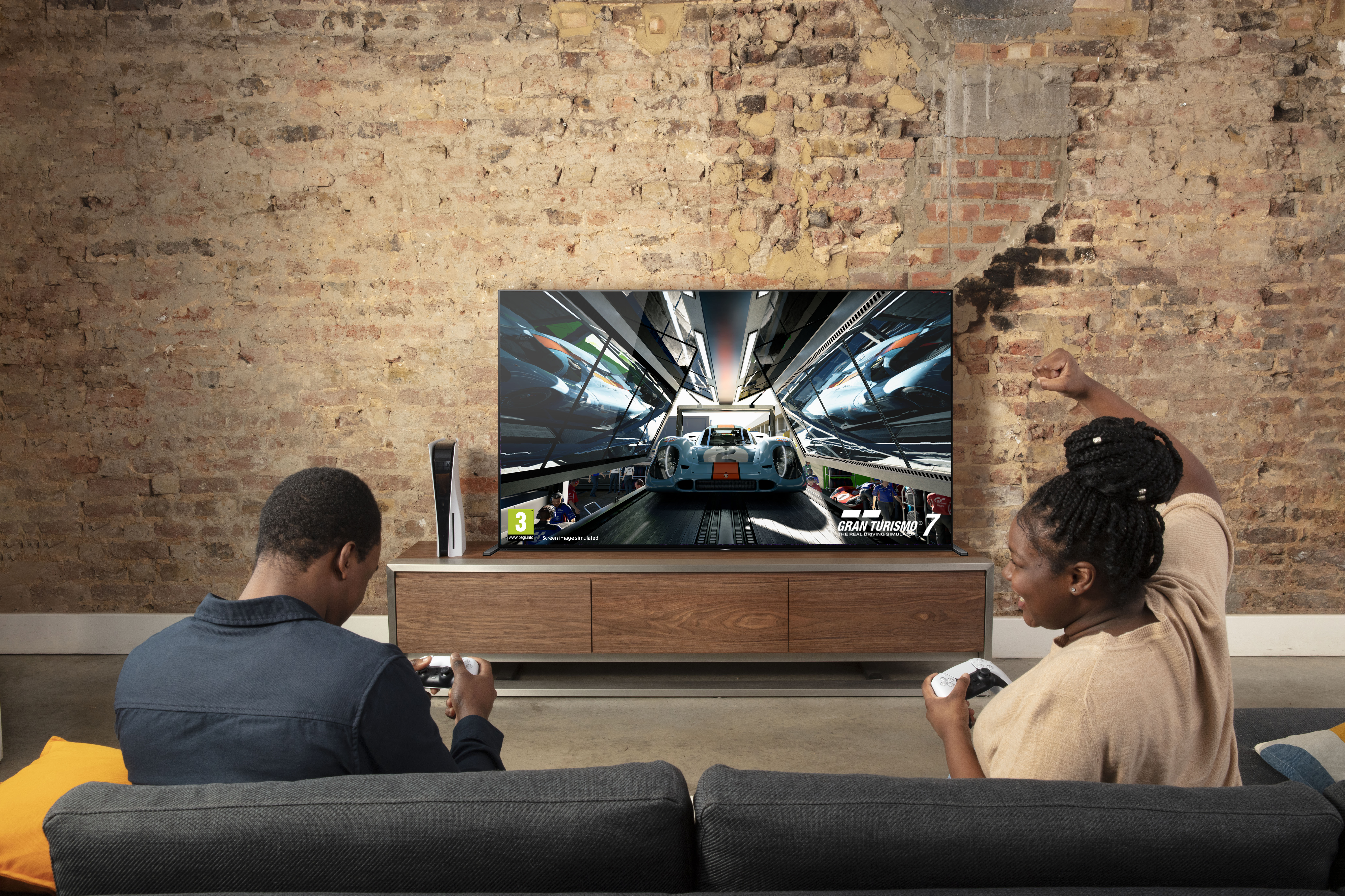 Zwei Personen spielen ein Spiel auf einem Fernseher, eine Konsole ist vorhanden.