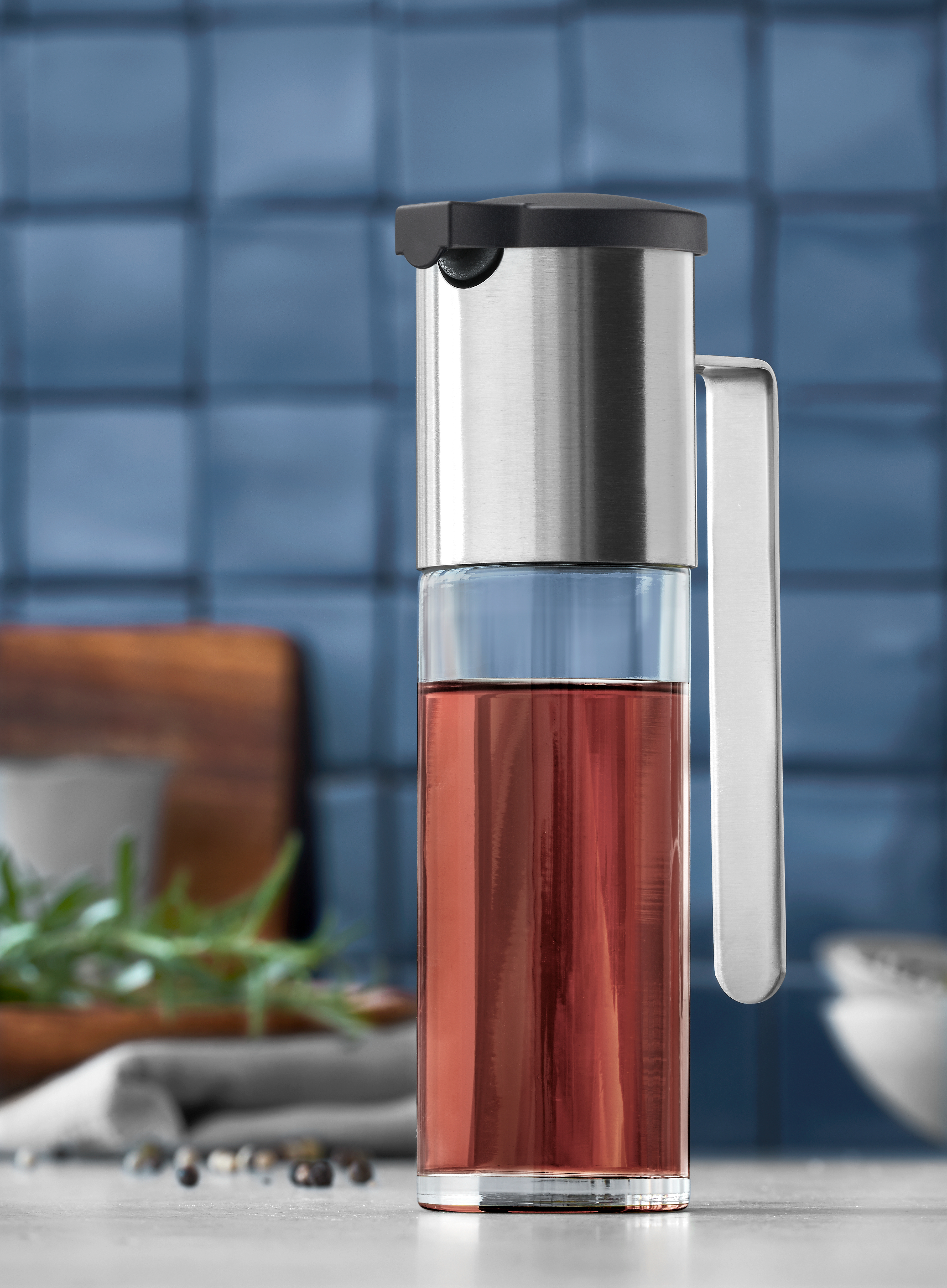 Ein Glas-Ölspender mit roter Flüssigkeit, Edelstahl-Details und schwarzem Deckel.