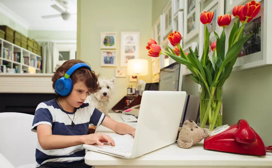 Jongen met koptelefoon gebruikt een laptop met een hond. Rode telefoon en bloemen op de achtergrond.
