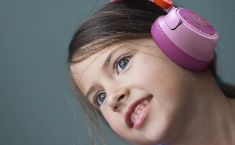 Een jong meisje met roze en paarse koptelefoon glimlacht lichtjes. Haar ogen kijken op met opwinding.