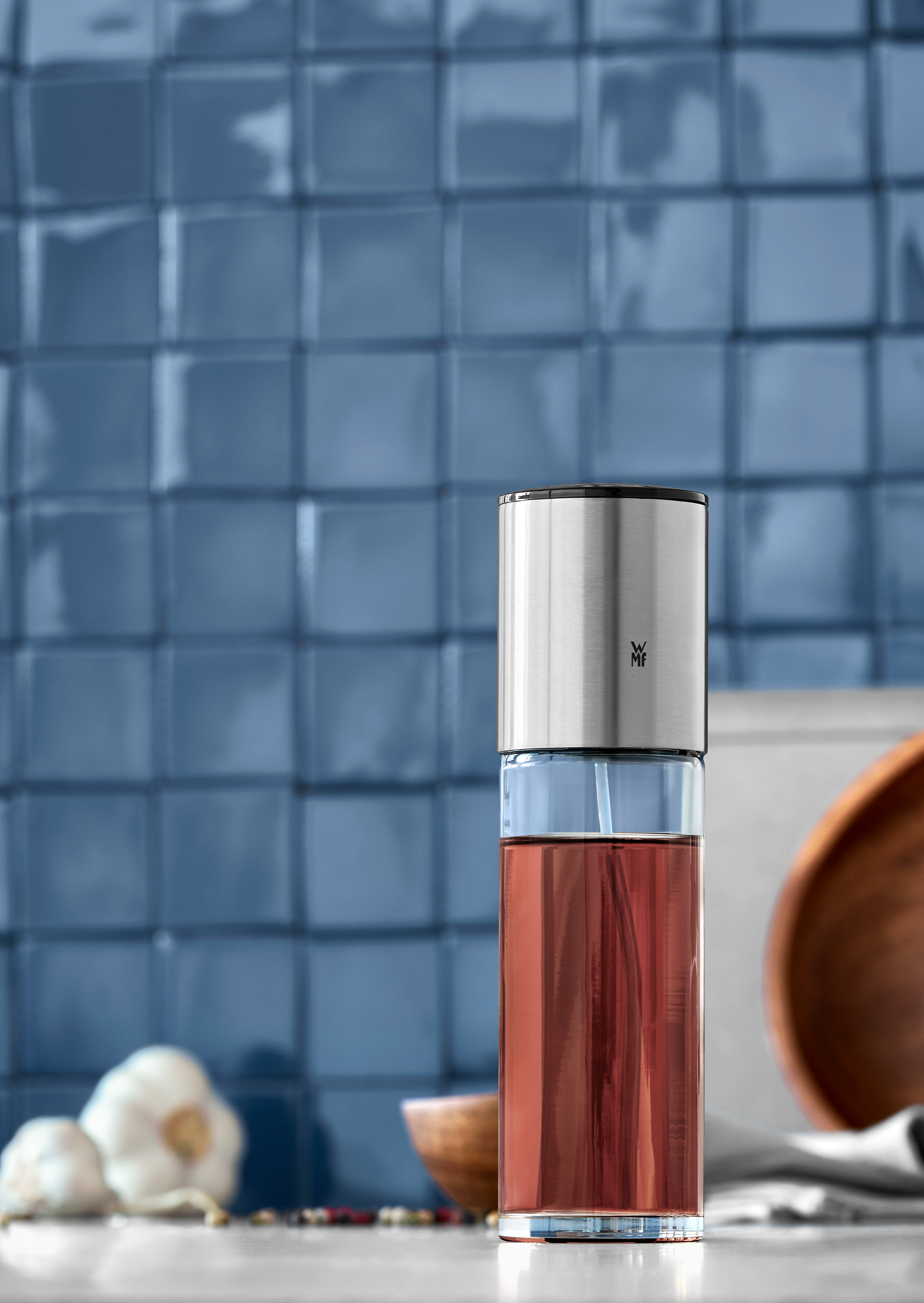 Glasflasche mit roter Flüssigkeit, auf blauem Fliesen-Hintergrund mit Knoblauch.