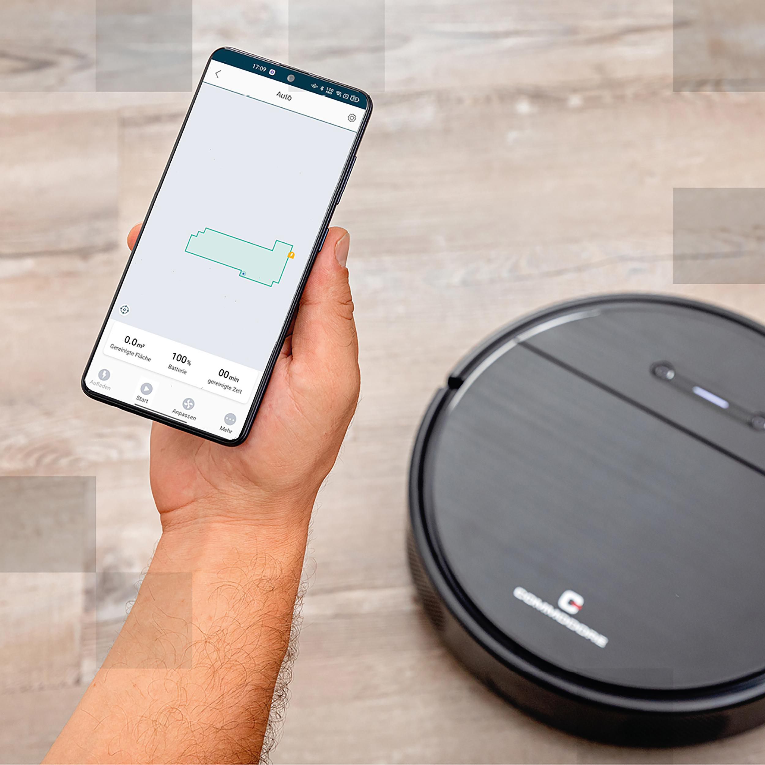 Hand, die ein Smartphone mit Reinigungsplan hält, neben einem schwarzen Roboterstaubsauger.