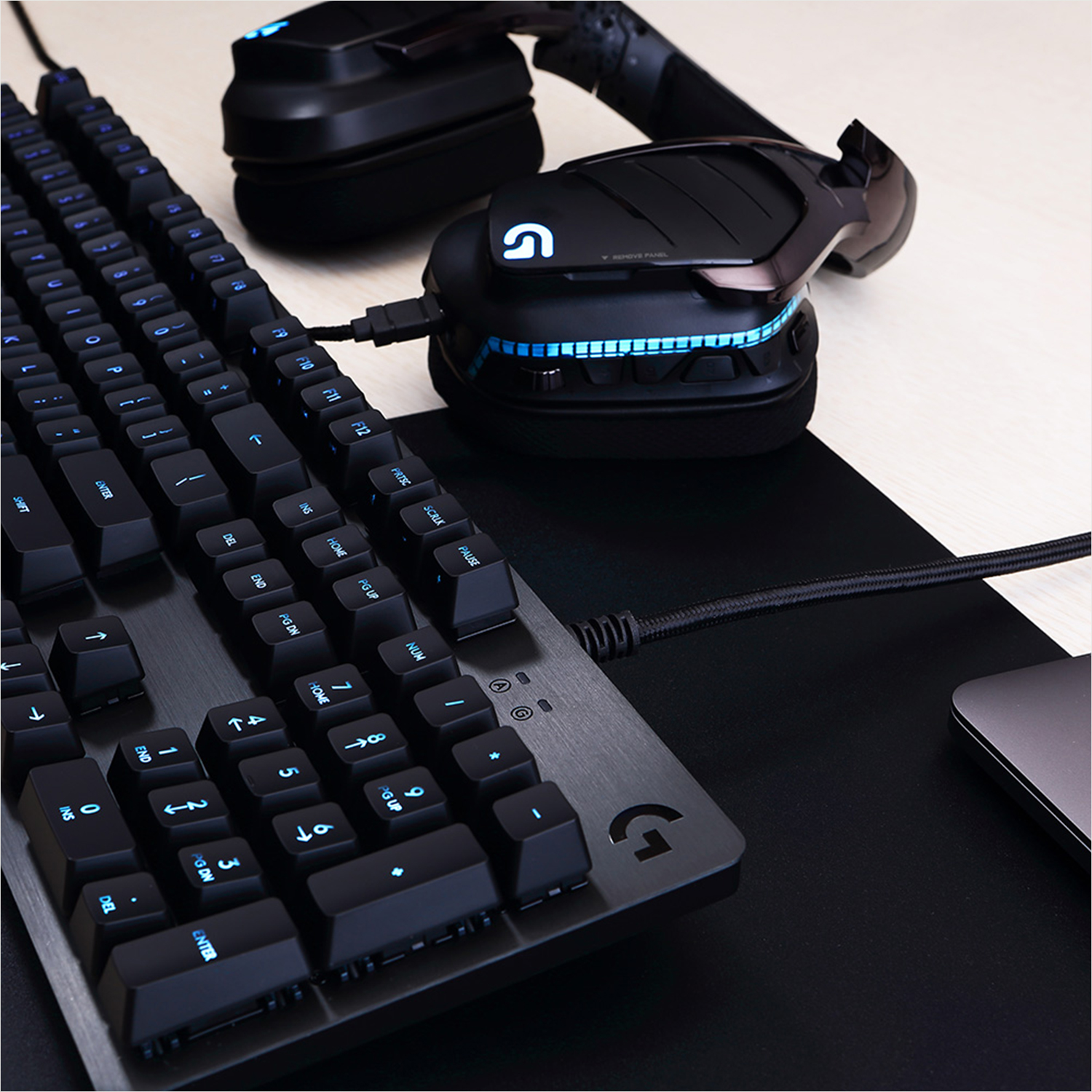 Gaming-Setup mit Tastatur und Headset. Tastatur blau beleuchtet. Schwarz und helles Holz.