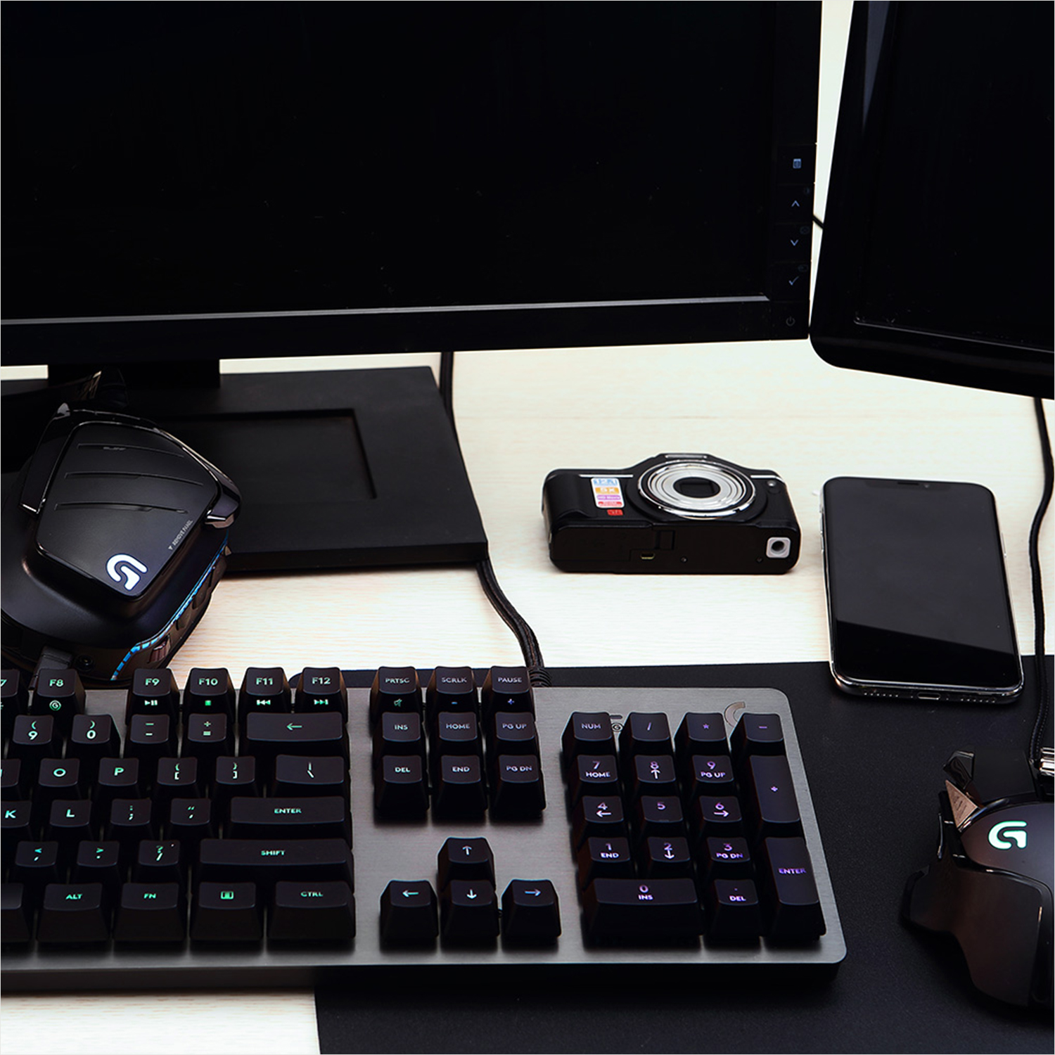 Gaming-Setup mit Tastatur, Maus, Kamera und Telefon. Schwarzes Mauspad und Monitor.