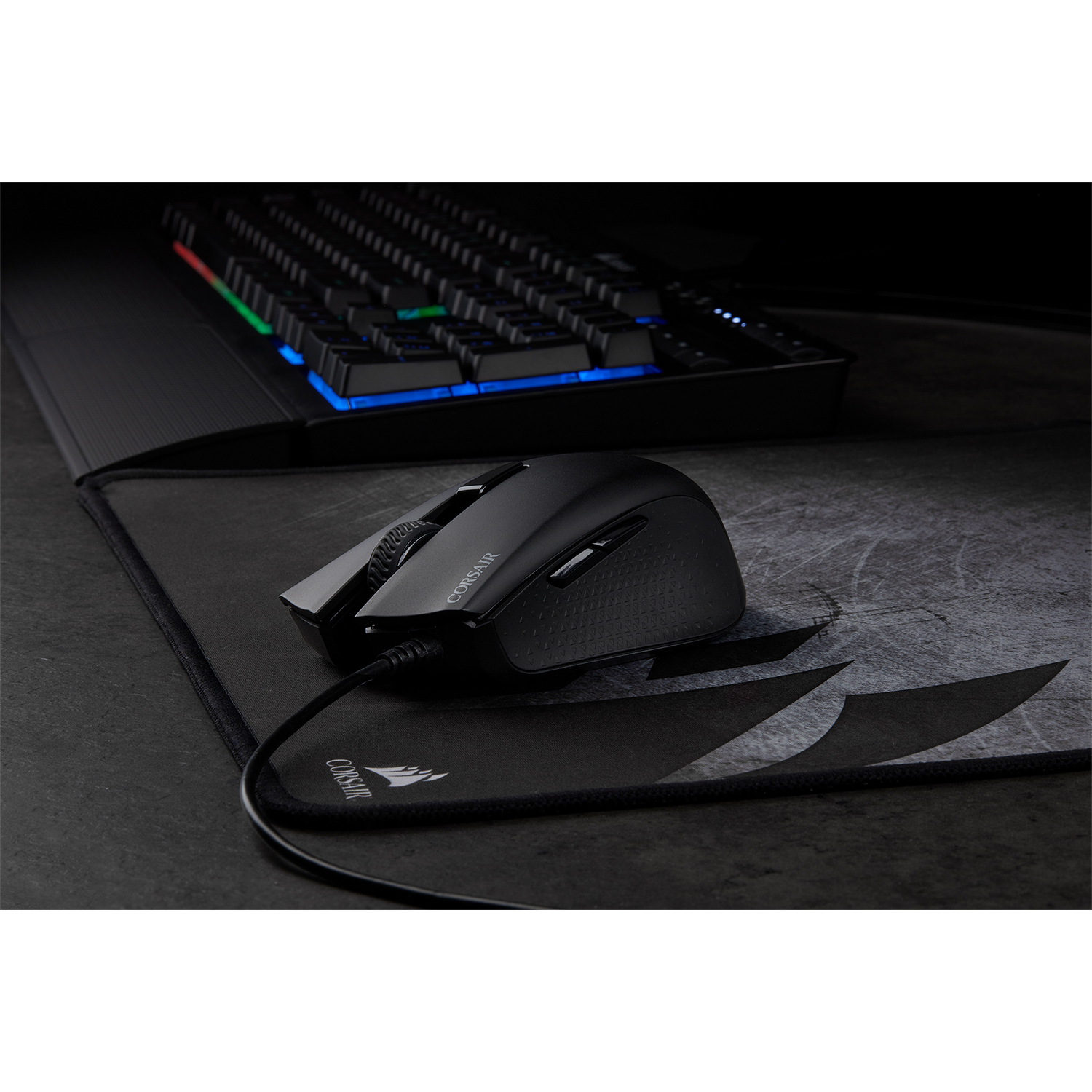 Un mouse e una tastiera neri su un tappetino nero. La tastiera ha tasti multicolore.