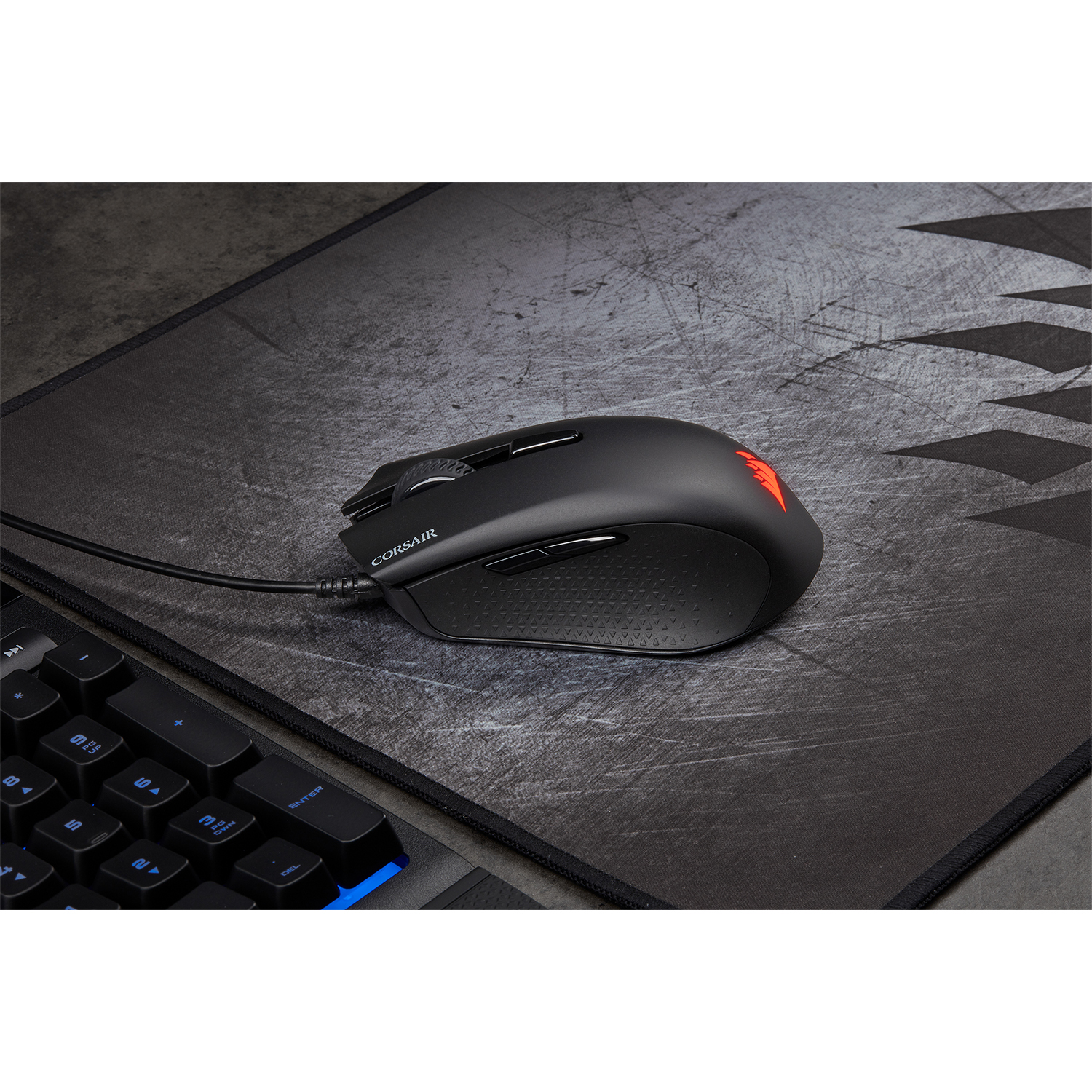 Mouse Corsair nero su un tappetino, accanto a una tastiera. Luce rossa.