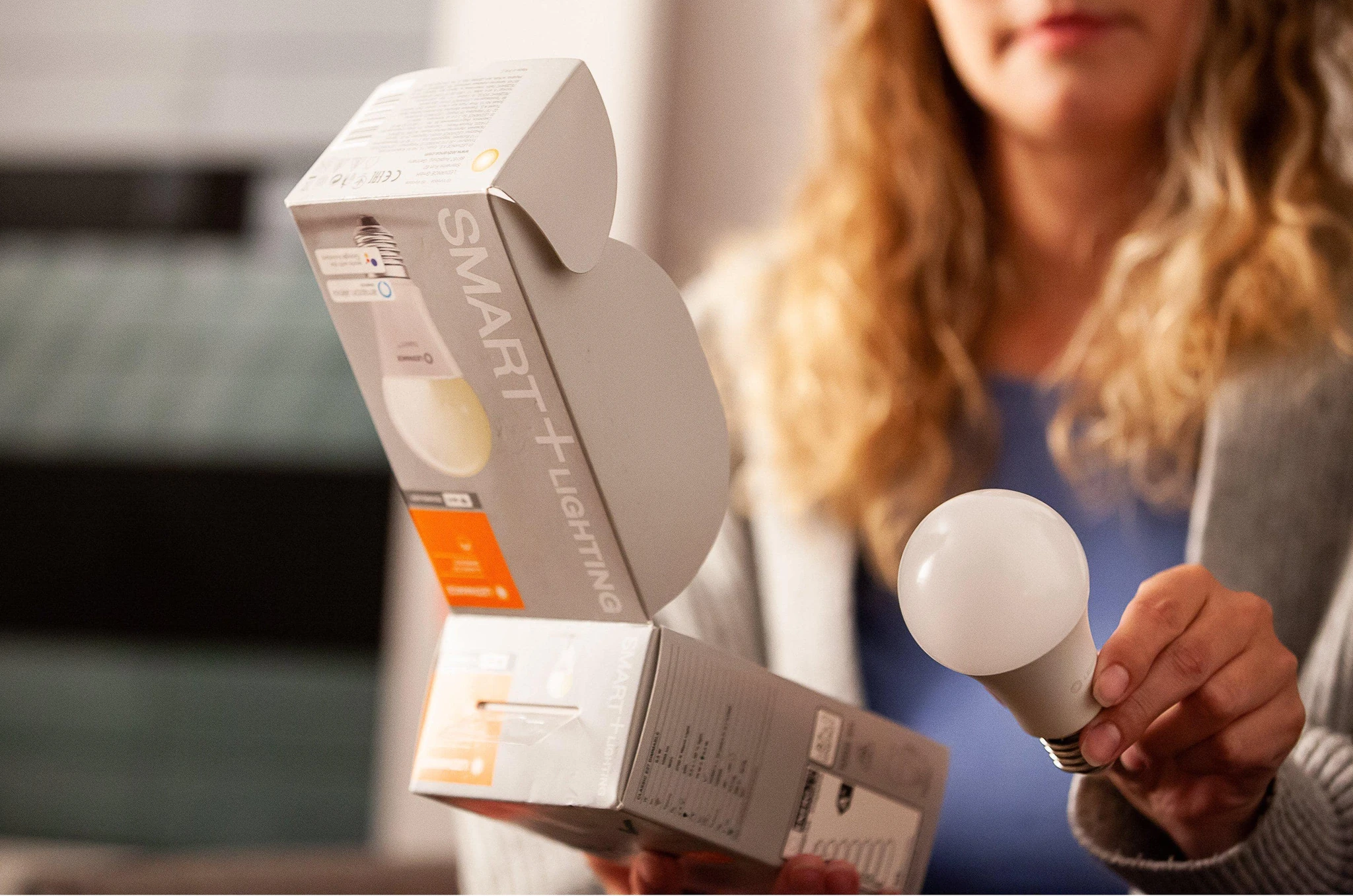Una donna tiene in mano una lampadina e apre una scatola di prodotti per illuminazione intelligente.
