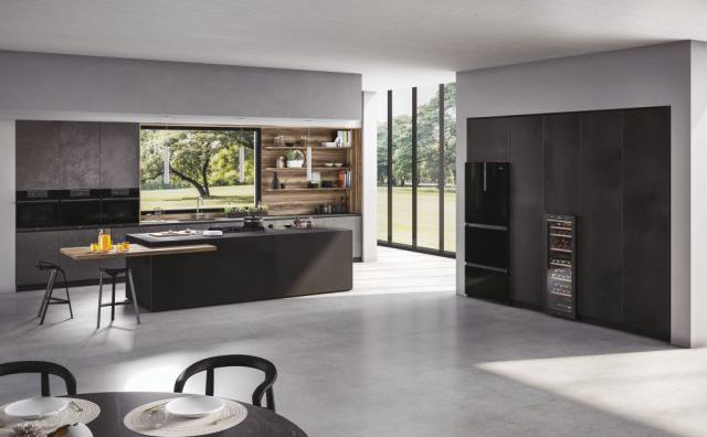 Cucina moderna con grande isola, scaffali in legno, elettrodomestici neri e ampie finestre con vista su un giardino.