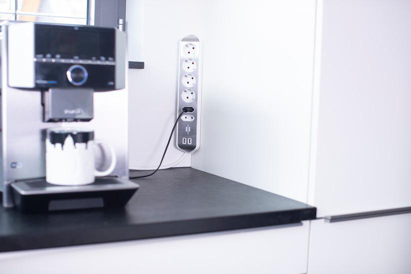 Küchenszene mit Kaffeemaschine, Steckdosenleiste und weißen Schränken.