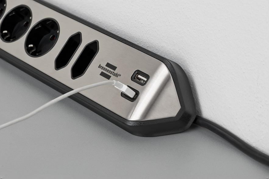 Eine Steckdosenleiste mit mehreren Steckdosen und einem USB-Anschluss. Ein weißes Ladekabel ist.