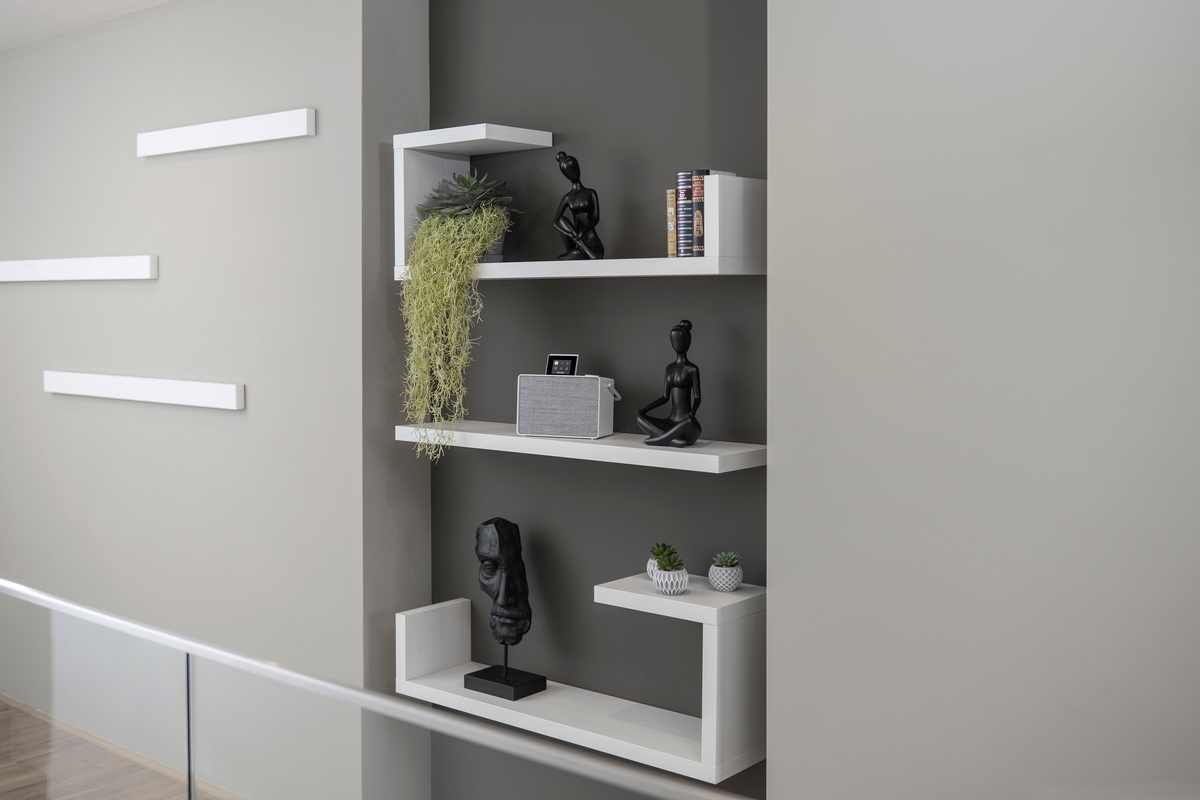 Étagères blanches avec décoration sur un mur gris. Livres, plantes et statues sont exposés.