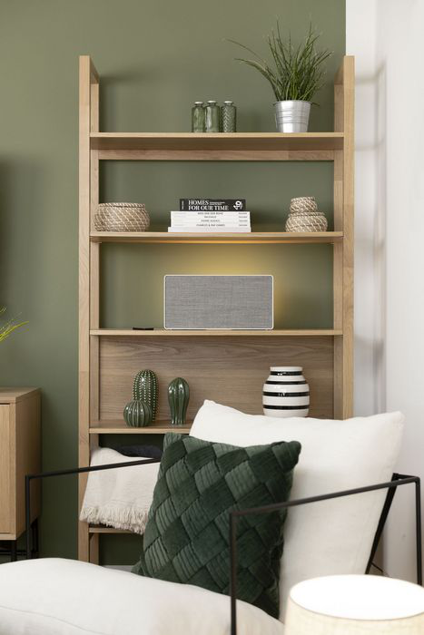 Regal aus Holz mit Büchern, Dekorationsartikeln und einem Lautsprecher. Davor steht ein grüner Sessel.