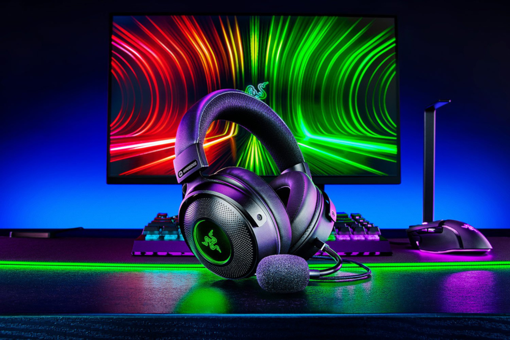 Gamingopstelling met Razer-koptelefoon, toetsenbord en muis. Verlichte monitor met een groene en rode gradiënt.
