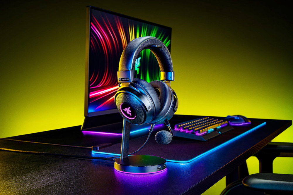 Zwarte gaming-koptelefoon op een standaard. Toetsenbord en monitor op de achtergrond.