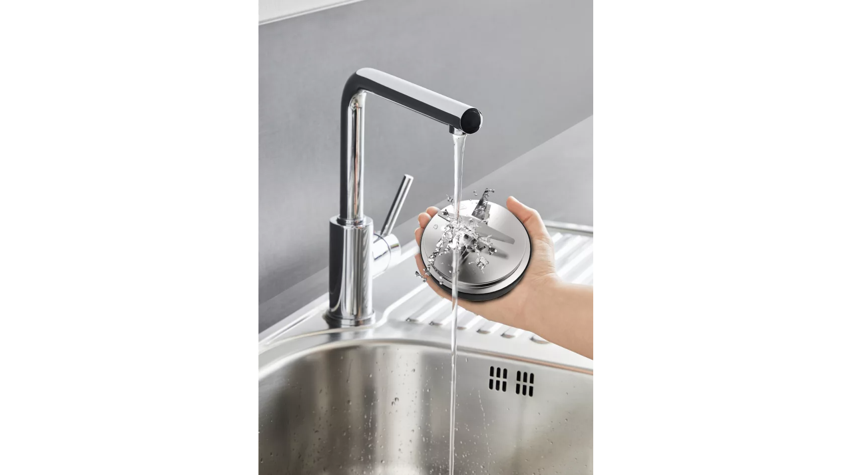A kitchen sink with a faucet, water running. A person is holding a metal food processor part under the water.