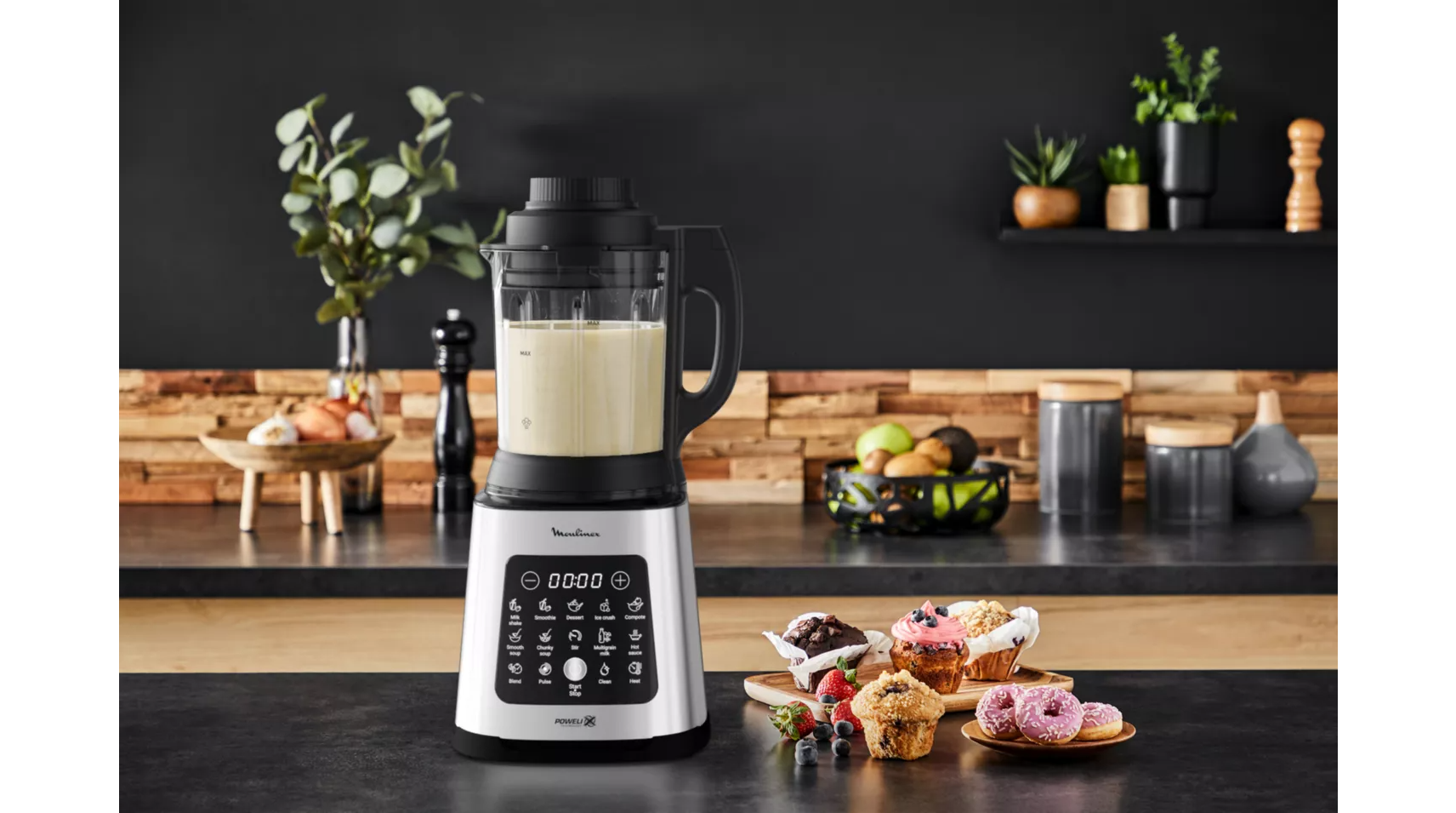 A blender with a digital display and muffins and donuts on the counter.