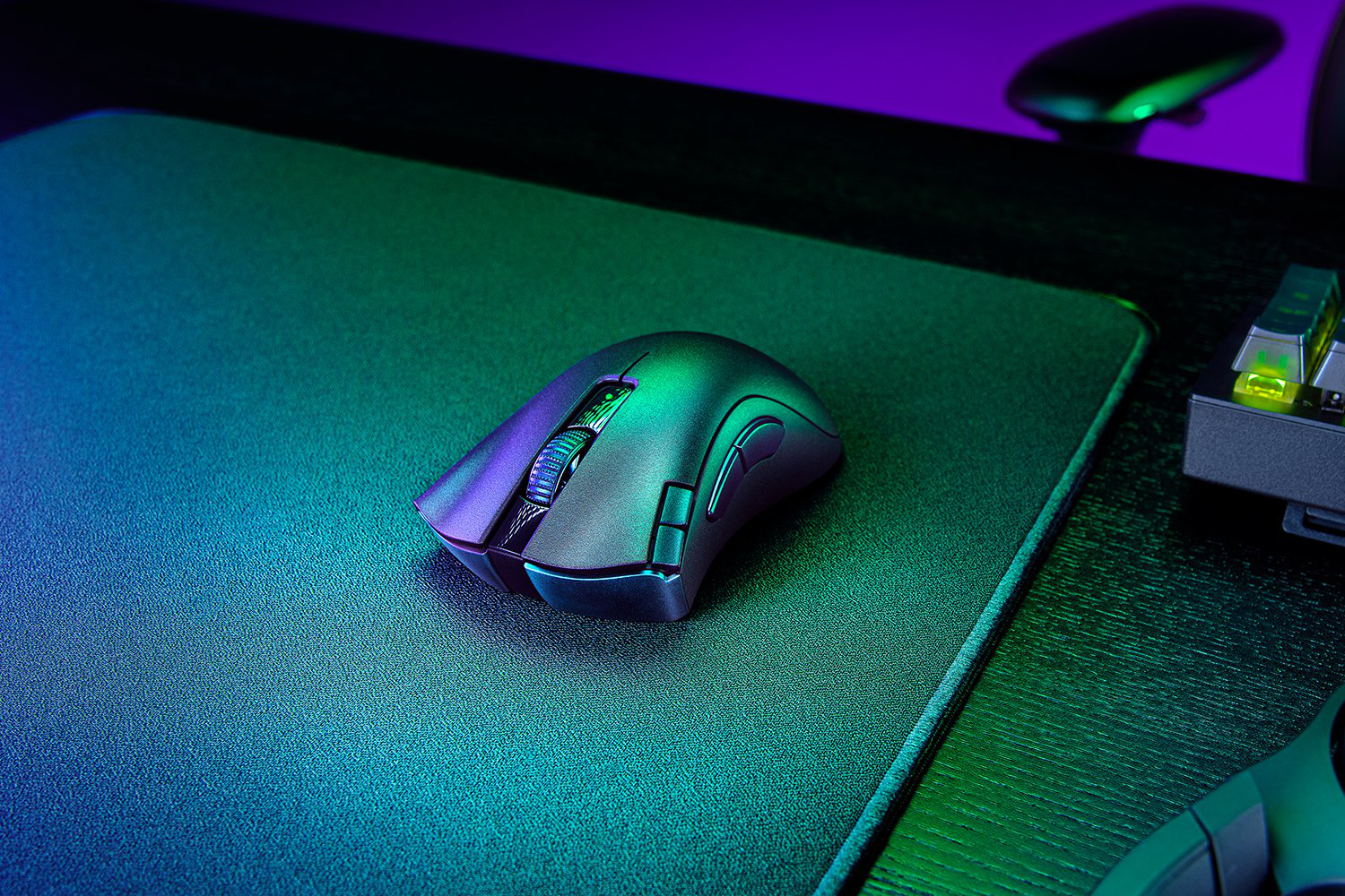 Eine schwarze Gaming-Maus auf einem grauen Mauspad, mit verschwommenem Gaming-Setup im Hintergrund.