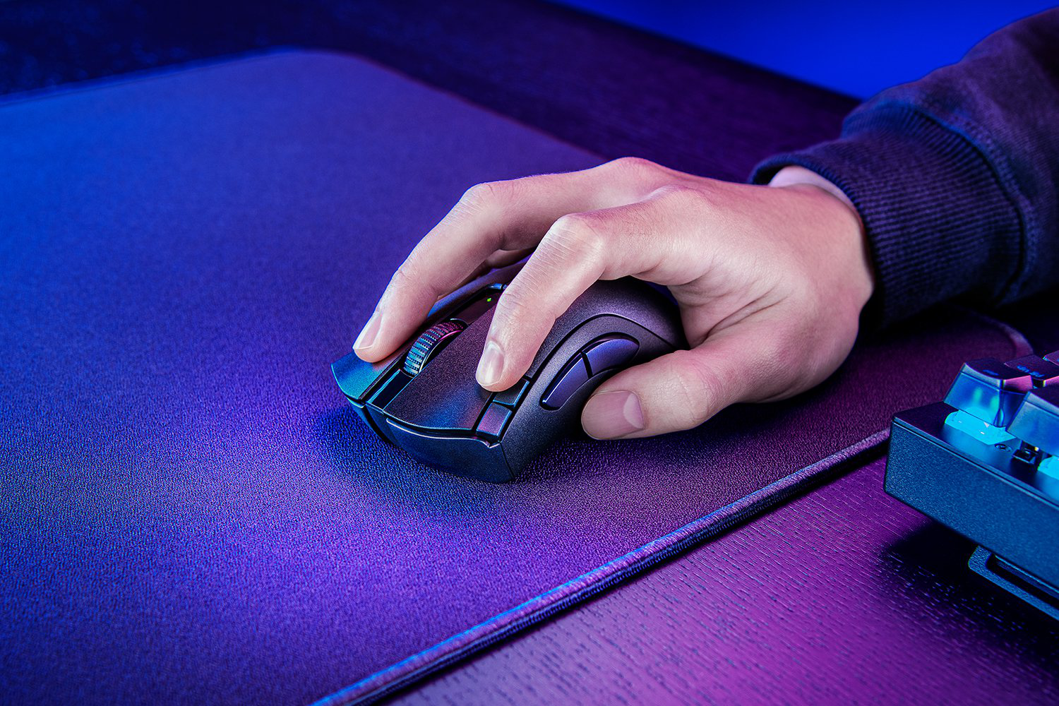 Eine Hand benutzt eine schwarze Maus auf einem blauen Mauspads, im Hintergrund eine Tastatur.
