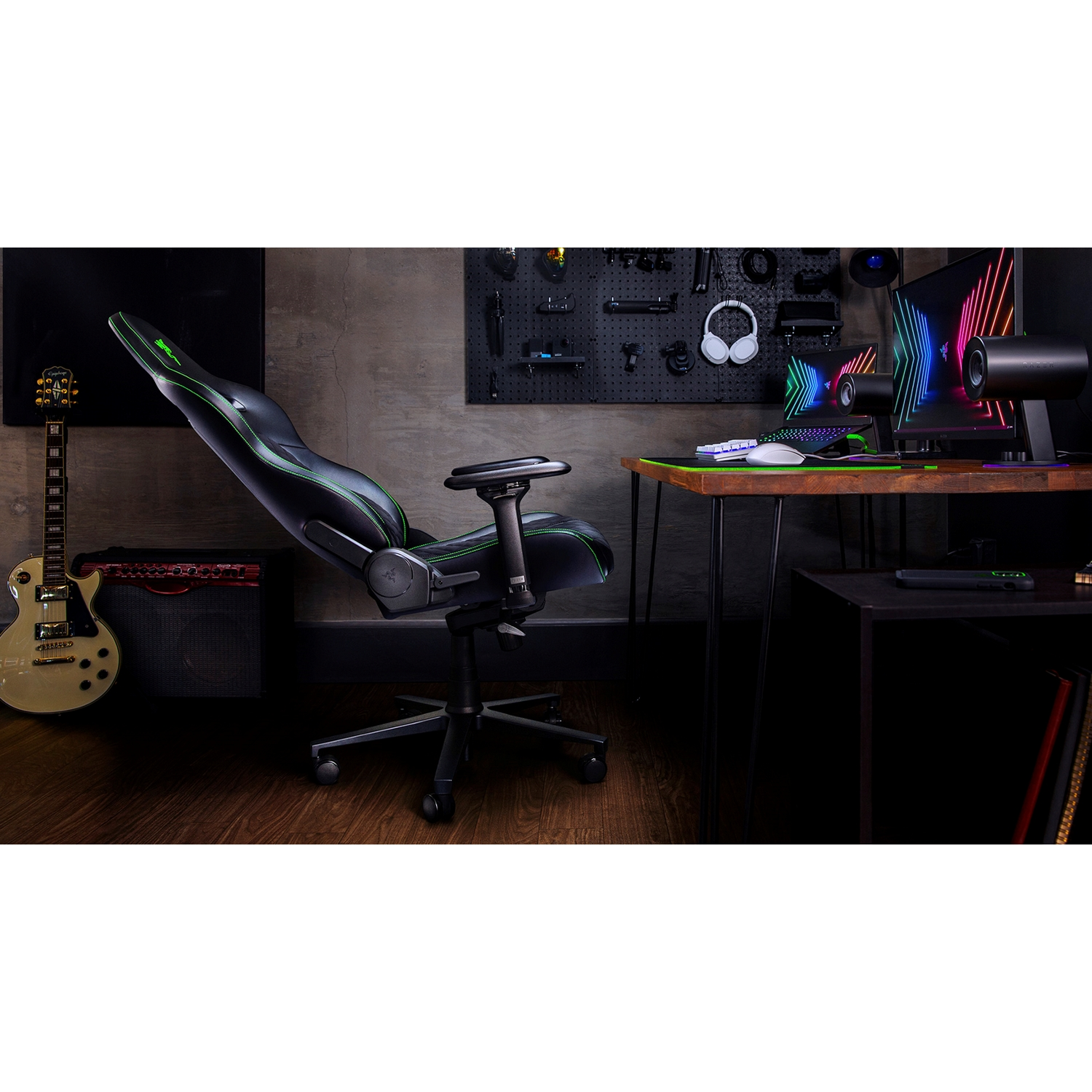 Configuración de juego con silla gamer negra y verde, guitarra, monitor, escritorio y accesorios.
