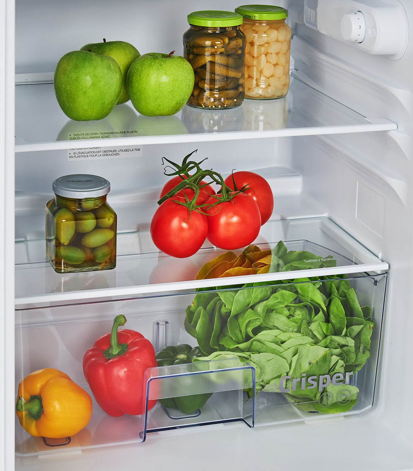 Refrigerator interior. Green apples, jars of food, tomatoes, and lettuce visible.