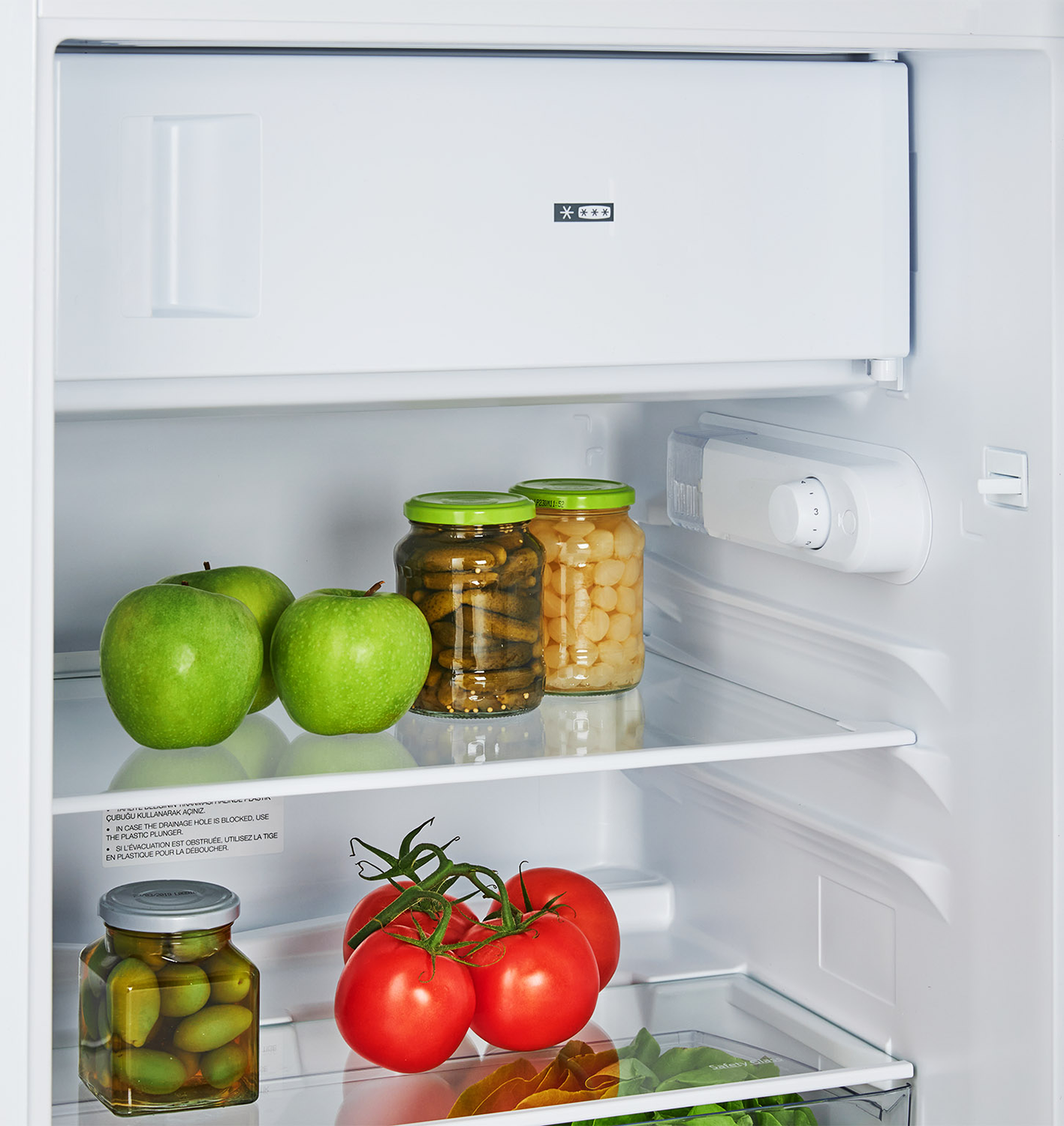 Fridge interior with green apples, jarred food, and tomatoes on shelves.