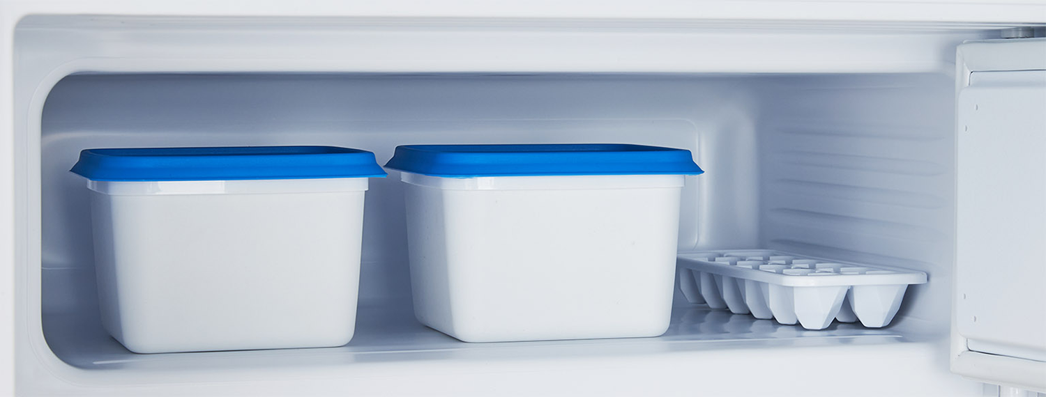 White containers with blue lids in a refrigerator. An ice cube tray is also inside.
