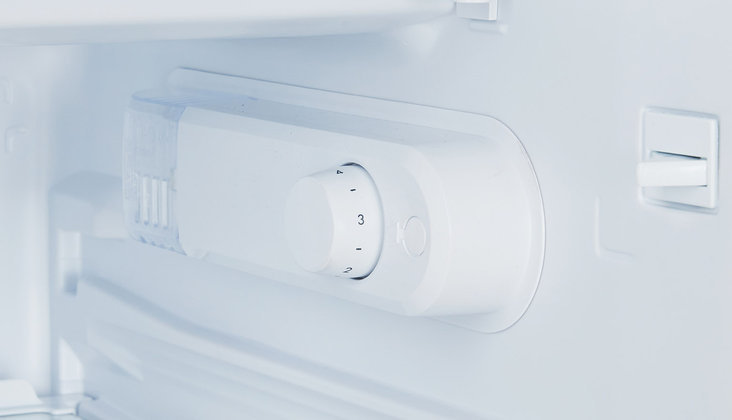 White refrigerator interior. A white control dial with numbers is visible.
