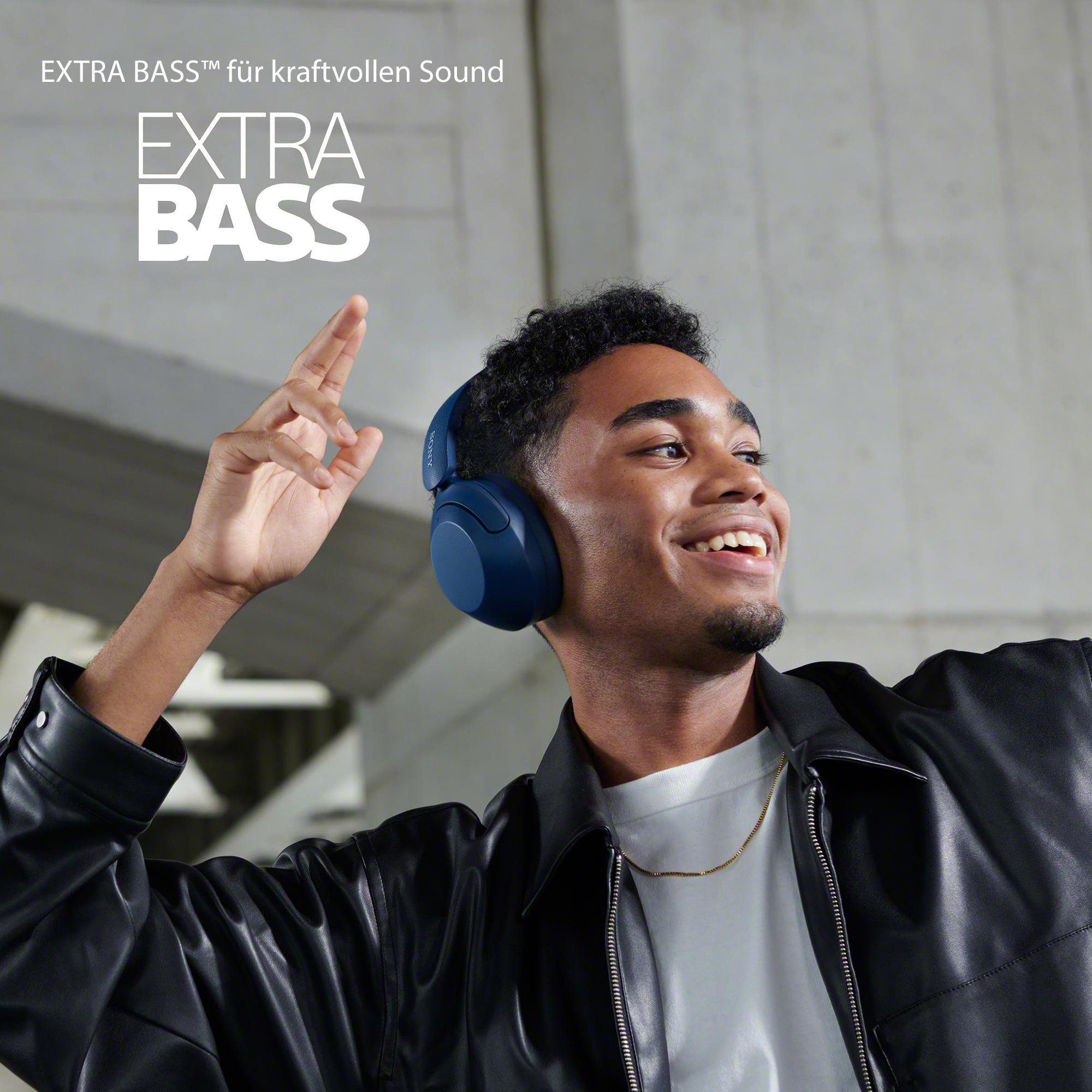 Ein Mann mit blauen Kopfhörern, lächelnd, mit EXTRA BASS Text, Lederjacke.