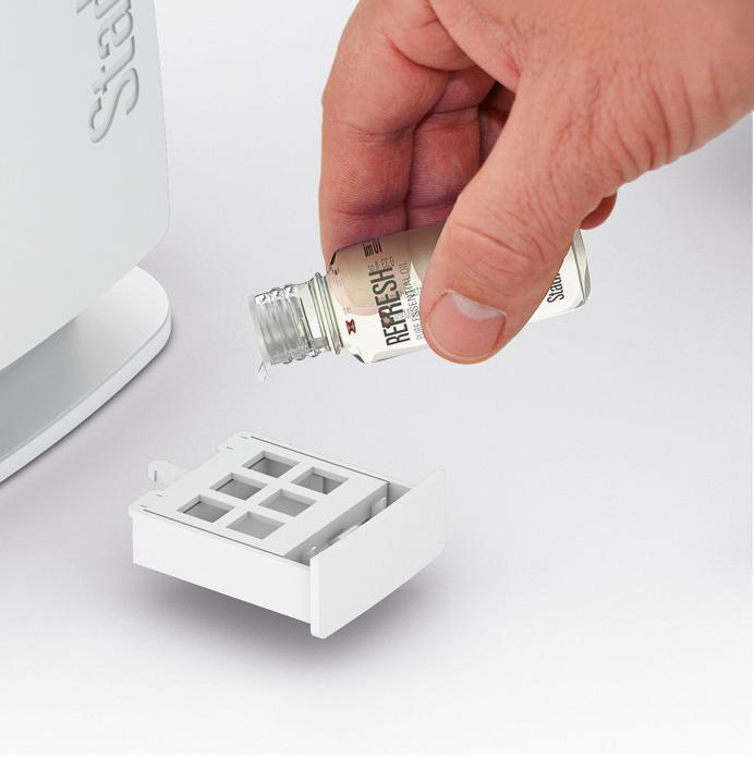 Die Hand einer Person gießt ätherisches Öl von Refresh in ein weißes Aromatherapiegerät.