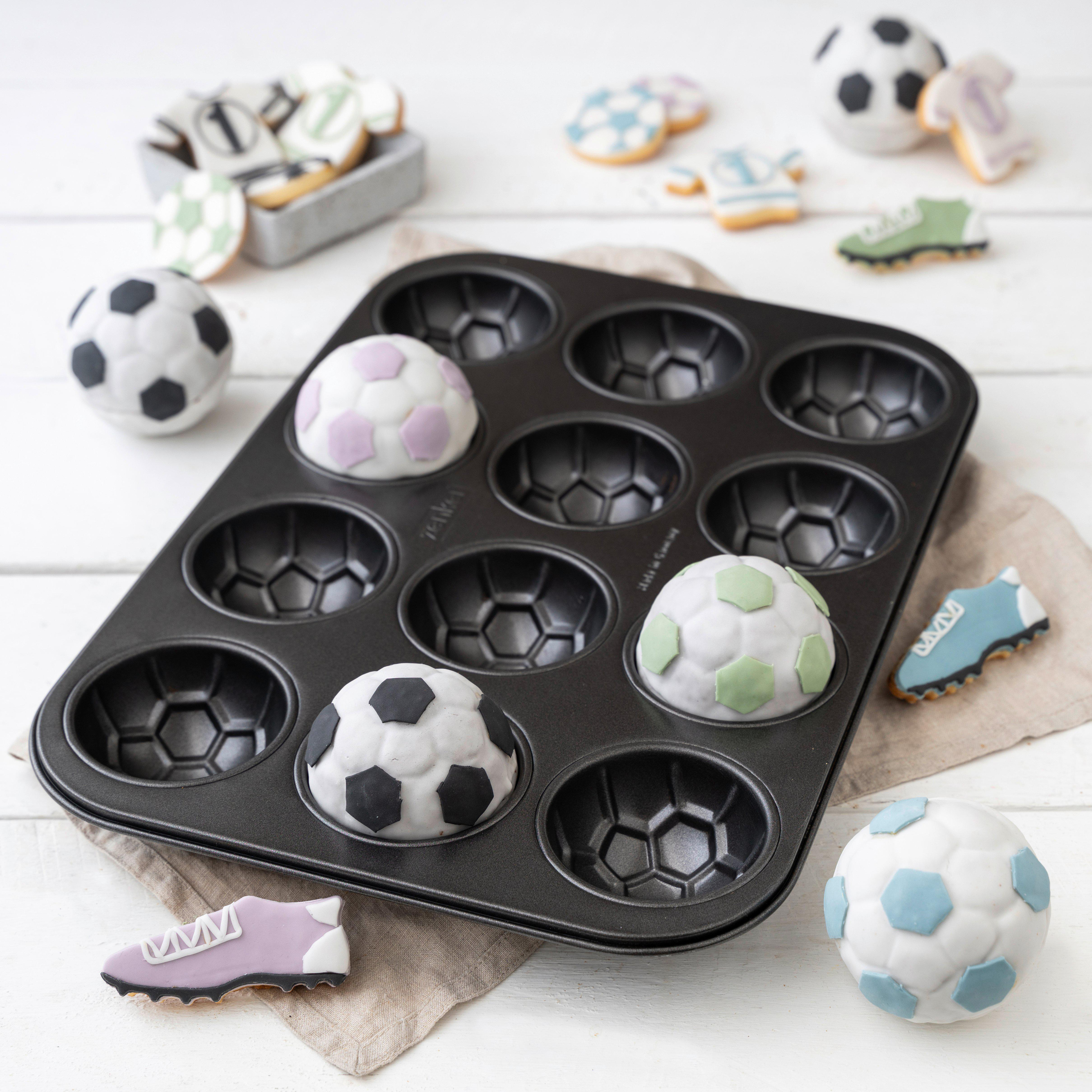 Muffinbackform mit Fußball-Muffins und Keksen in Fußball- und Trikotform auf weißem Tisch.