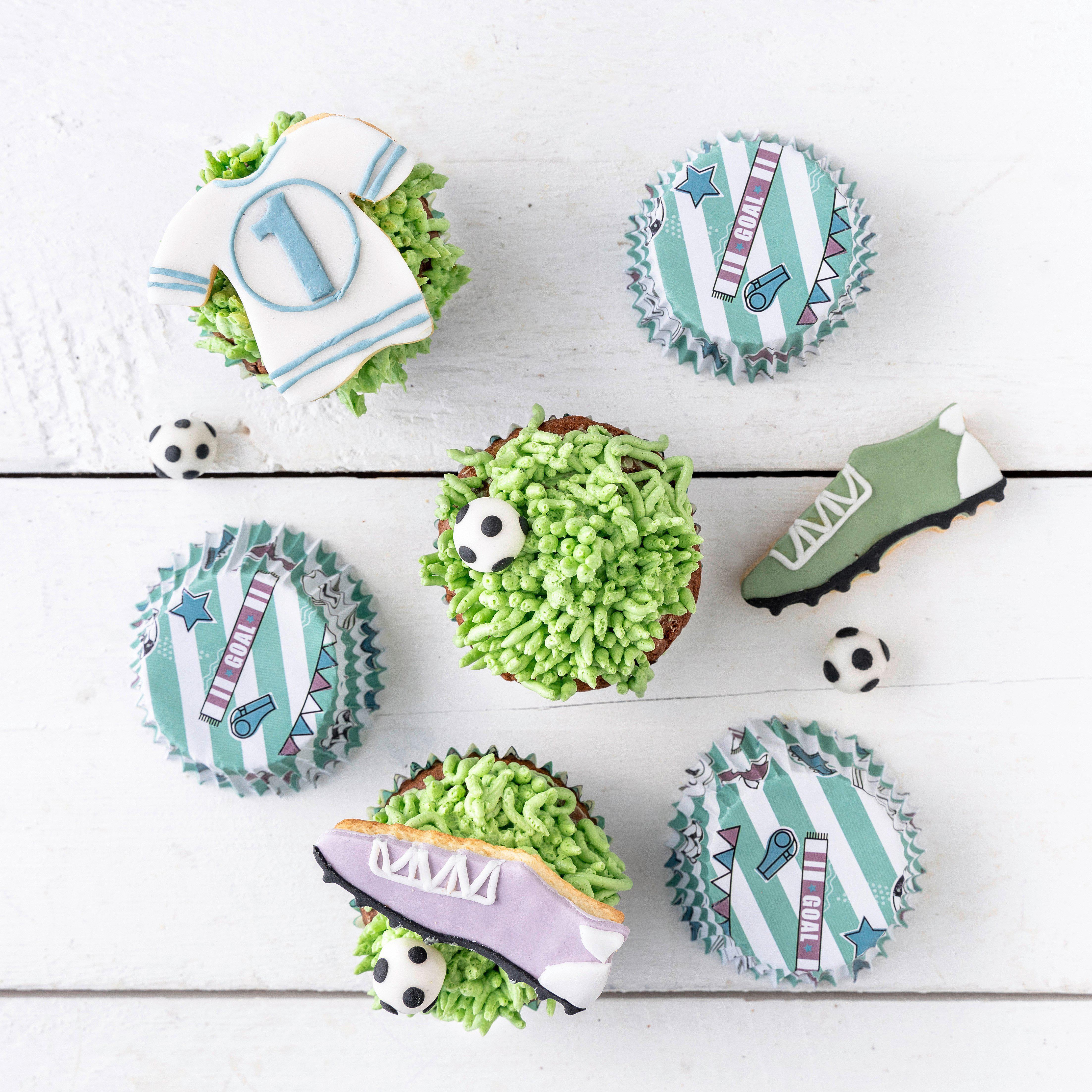 Mit Fußballmotiven dekorierte Cupcakes auf weißer Holzoberfläche.