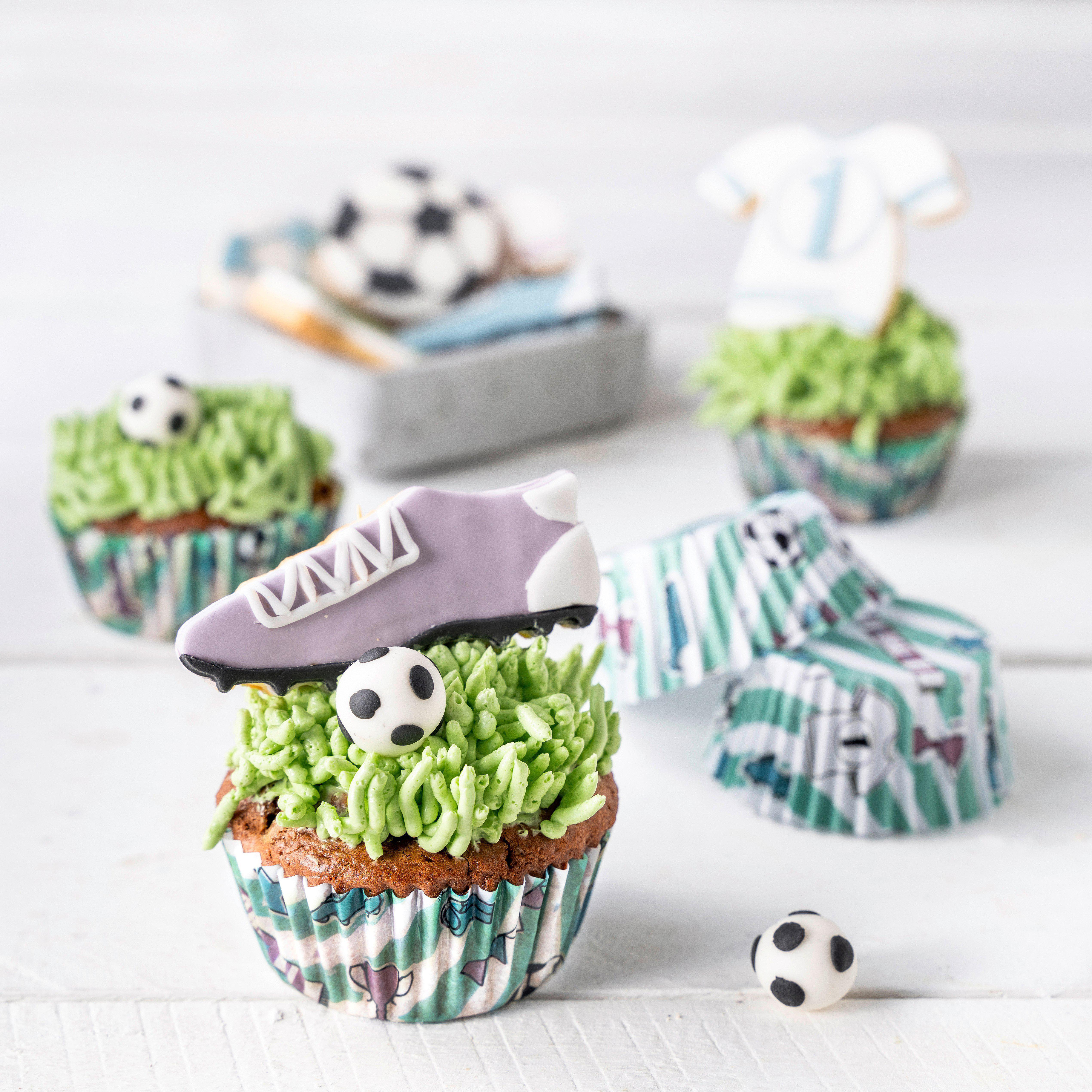 Cupcakes mit Fußball-Thema. Fußball, Schuh, Trikot-Toppings auf grünem Zuckerguss. Weißer Hintergrund.
