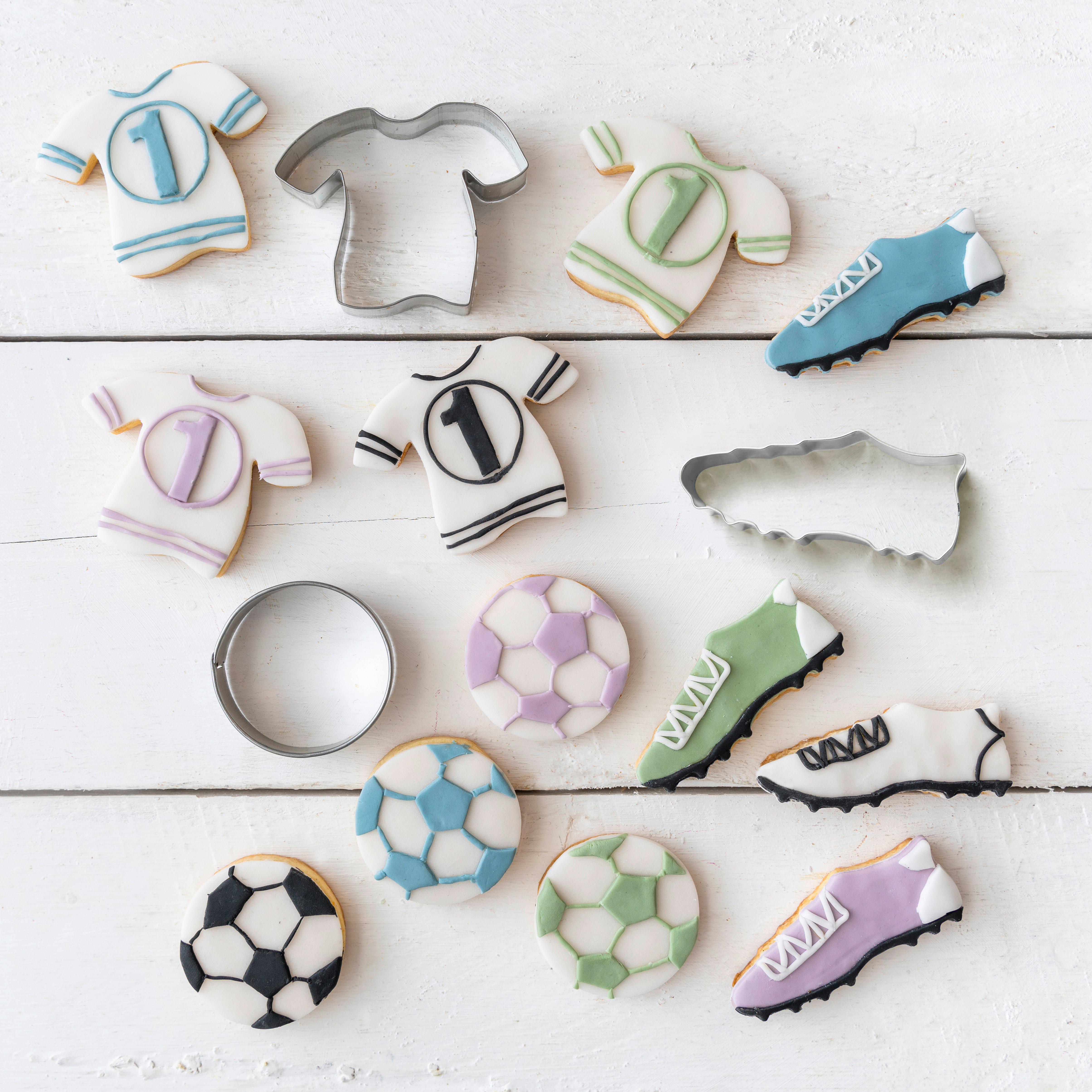 Fußball-Cookies und Ausstecher auf einer weißen Holzoberfläche.