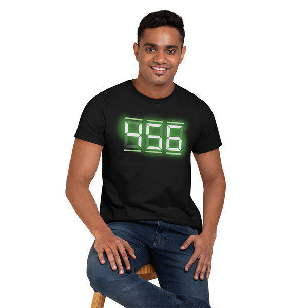 Mann trägt ein schwarzes T-Shirt mit digitaler Anzeige '956'. Er sitzt auf einem Hocker und lächelt.