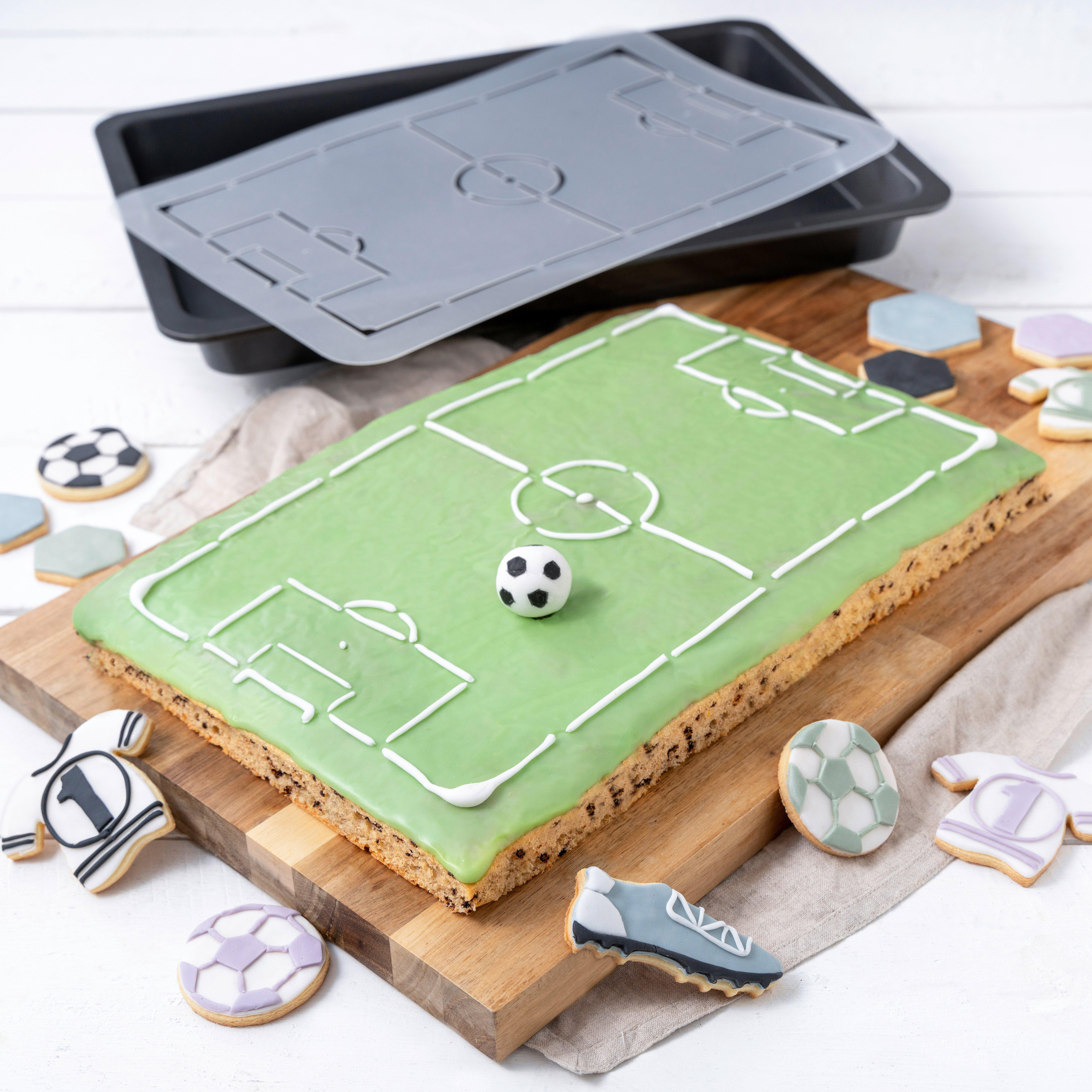 Ein rechteckiger Kuchen, dekoriert als Fußballfeld mit Zuckerguss, kleinem Fußball und passenden Keksen.