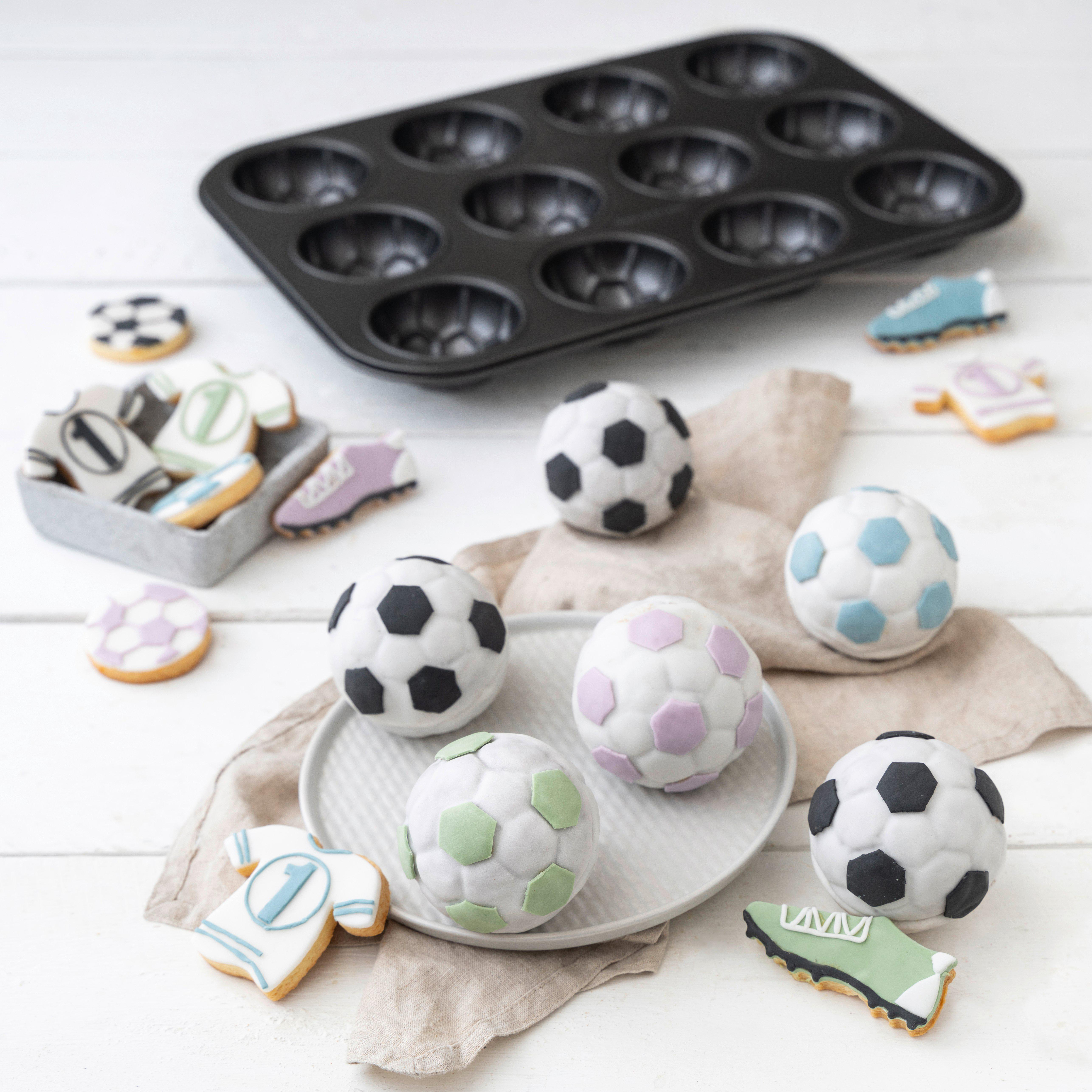 Fussball-Muffins und Kekse in Trikot- und Schuhform auf weissem Tisch mit Muffinblech.