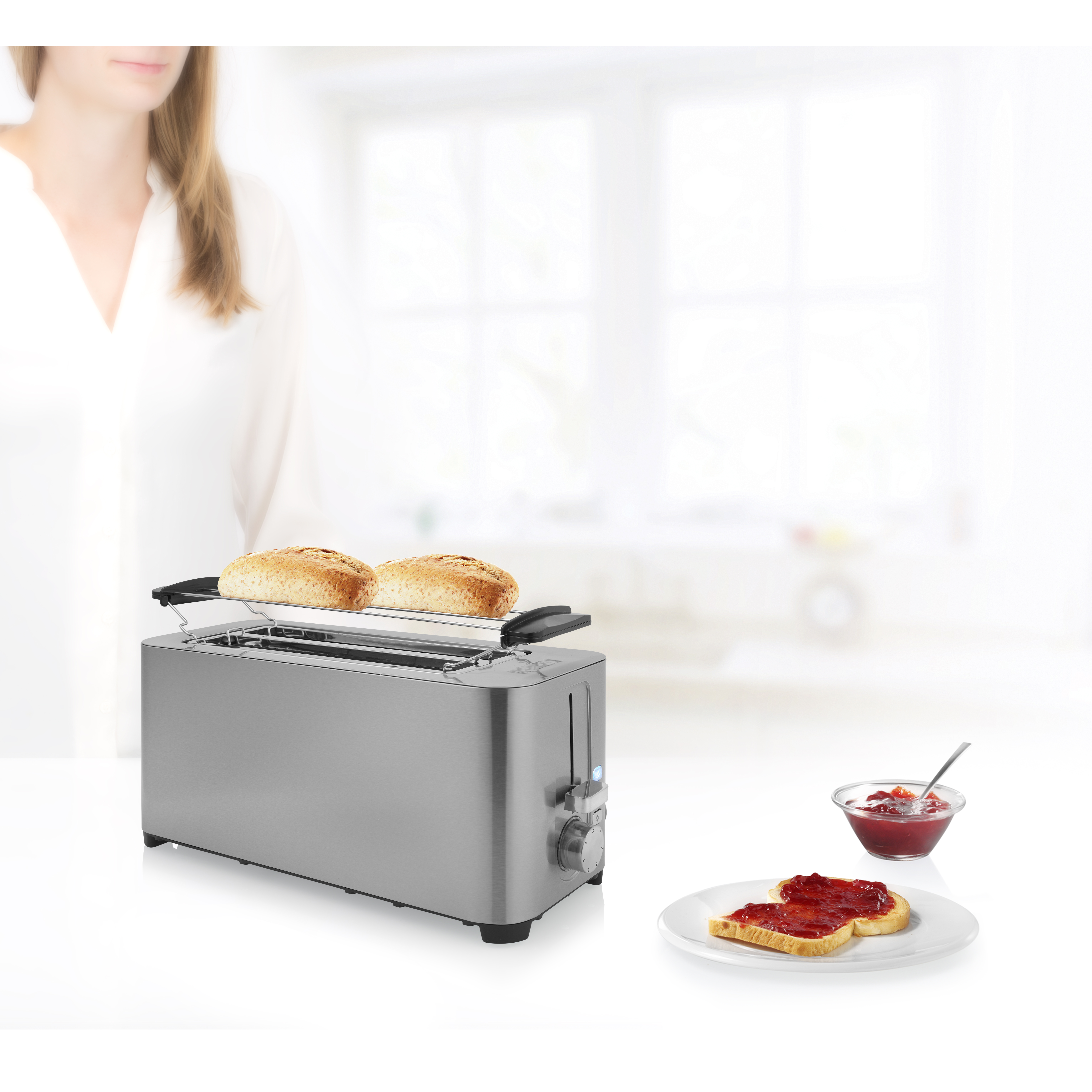 Zilveren broodrooster met twee sneetjes toast, jam en een vrouw op de achtergrond.