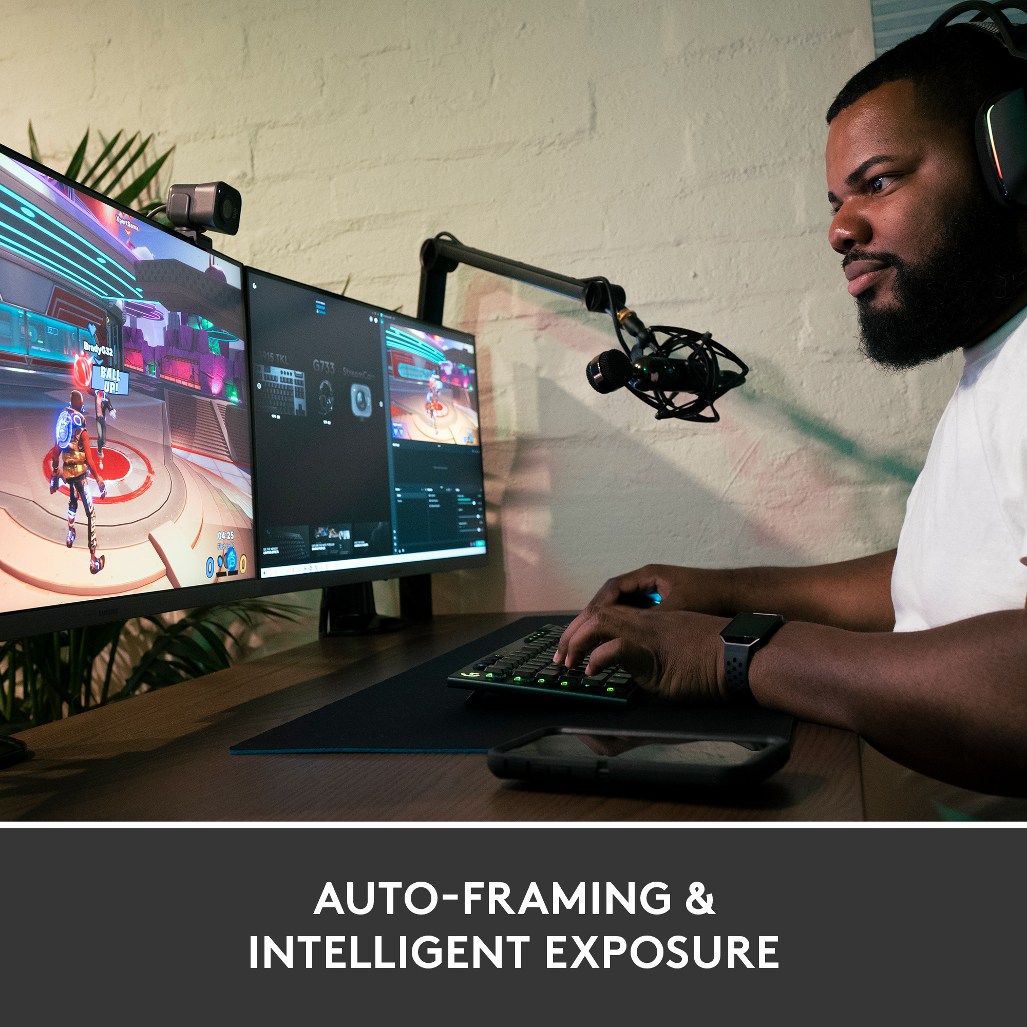 Ein Mann benutzt einen Computer mit zwei Monitoren. Ein Mikrofon ist vor ihm. Text: 'AUTO-FRAMING & INTELLIGENT EXPOSURE'.