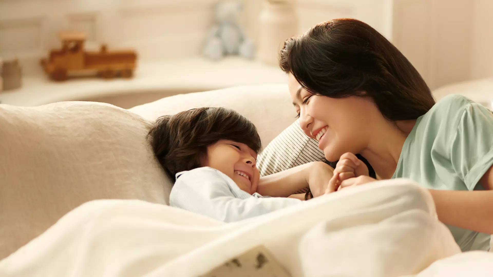 Mother and child in bed, smiling. The child is looking at his mother.