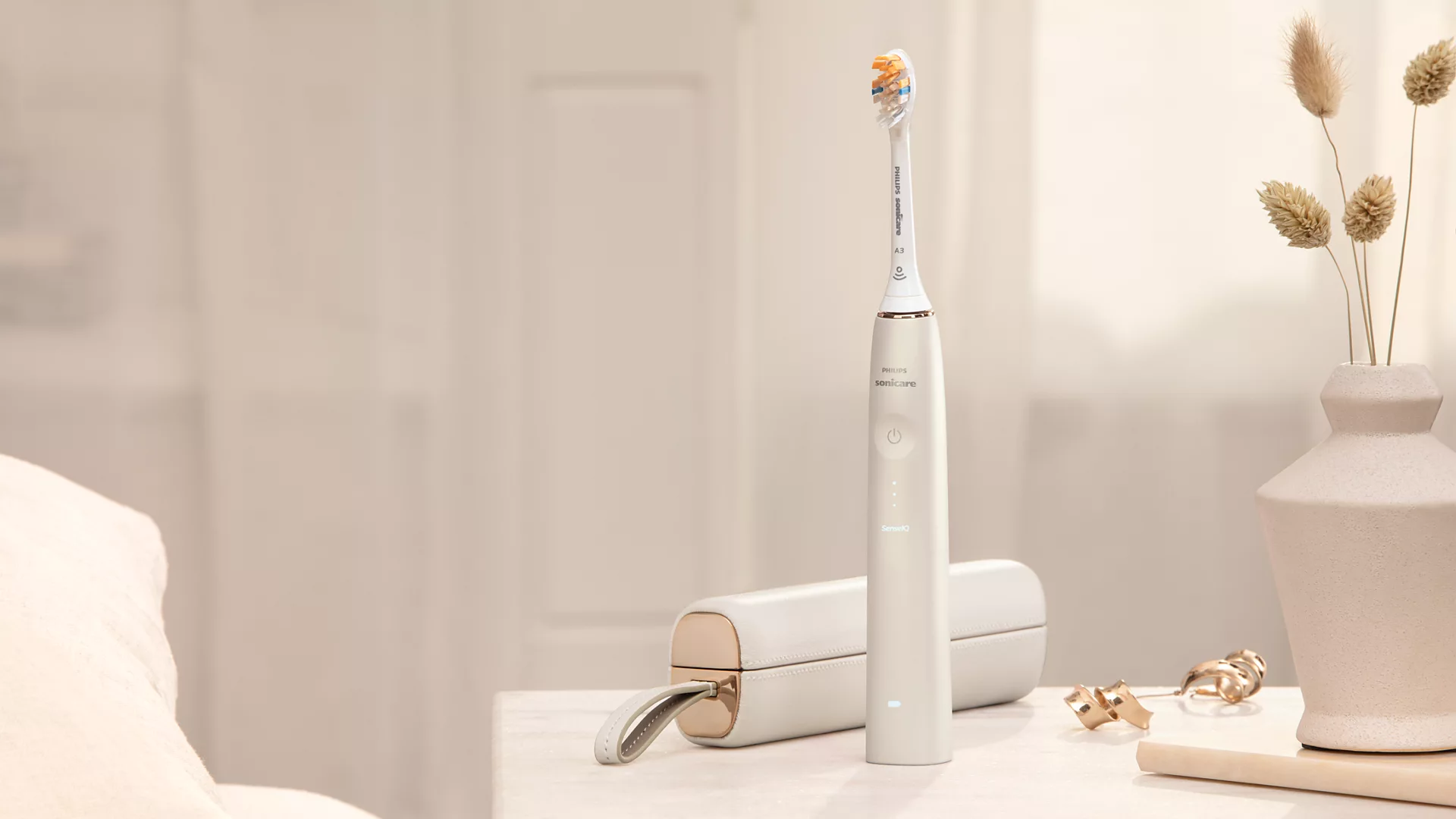 A white and gold electric toothbrush with a charging case and accessories on a table.