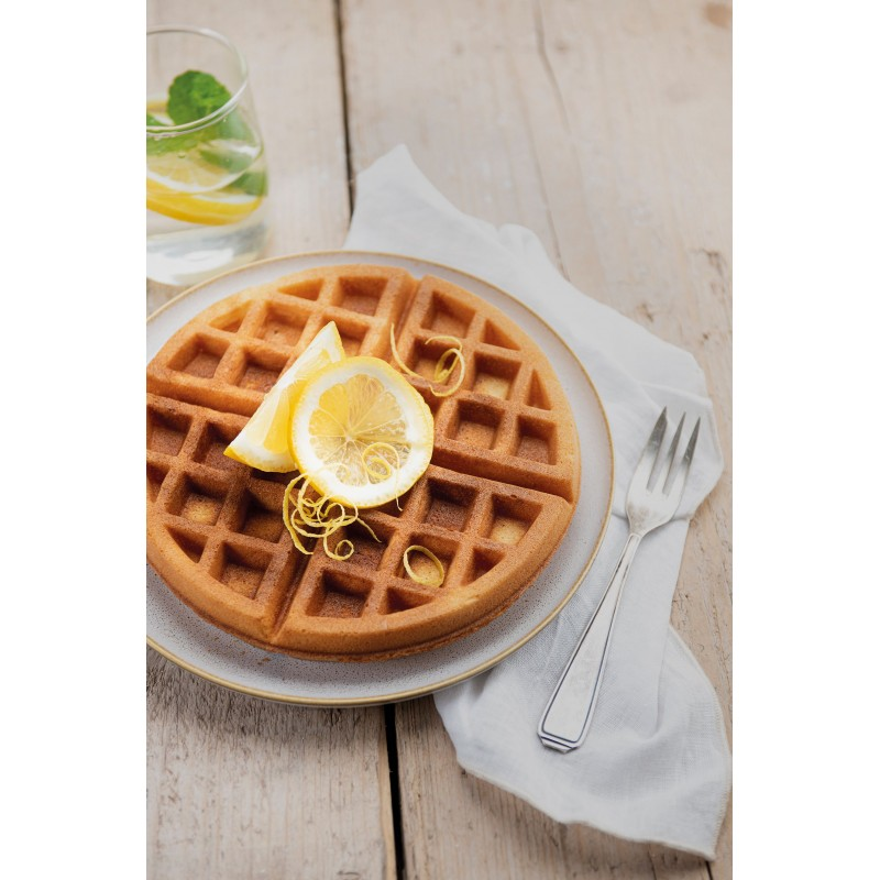 Een ronde wafel met citroenplakjes op een bord, naast een glas water en een vork.